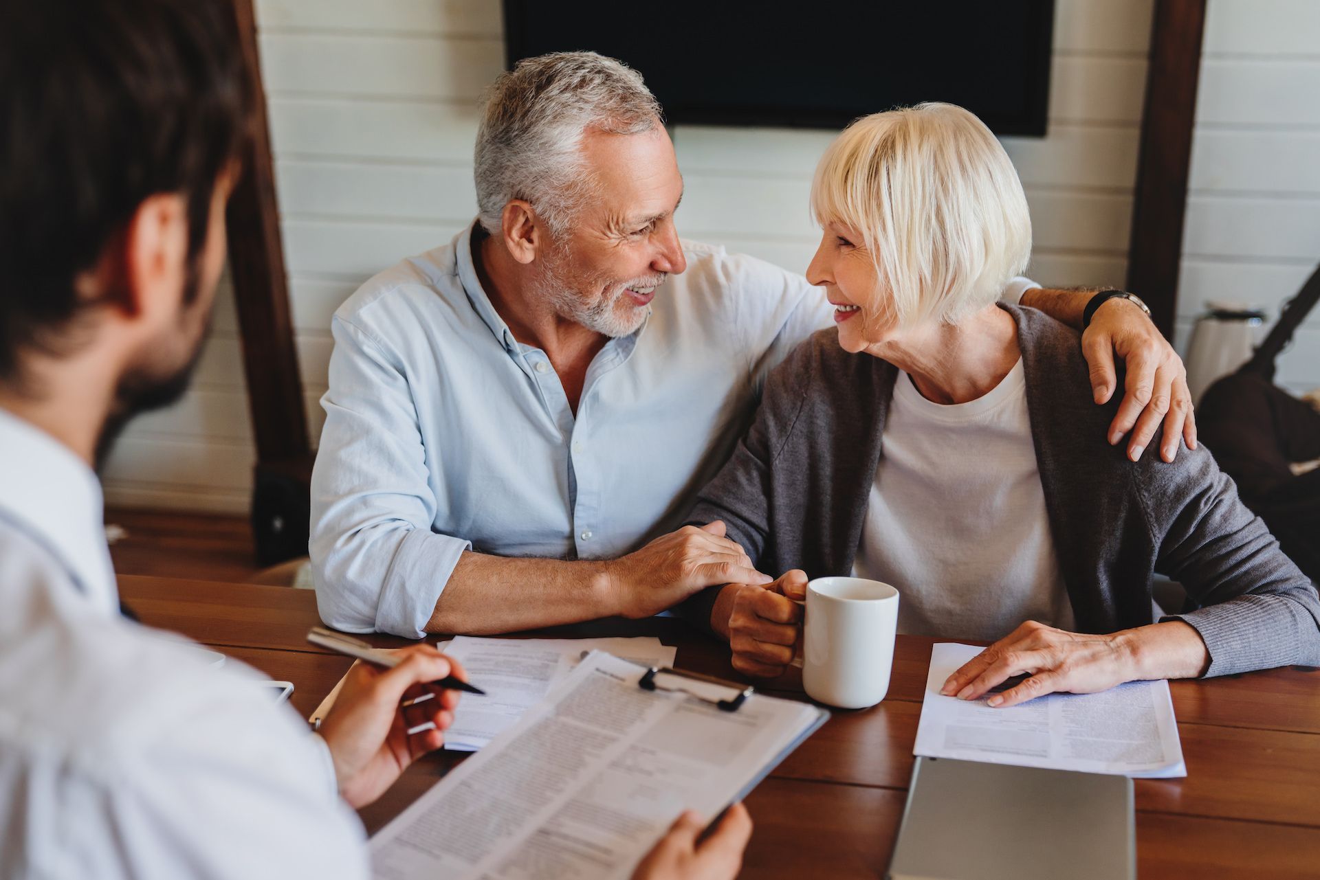 Older couple smiling, arm around each other, meeting with advisor at a table, reviewing paperwork.