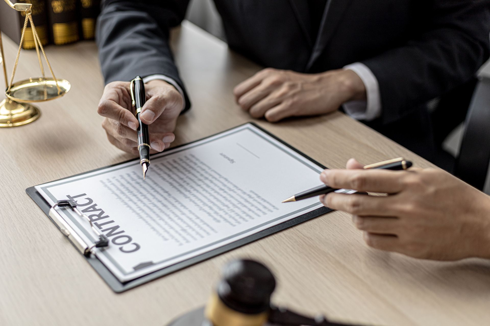 Two people reviewing and pointing at a contract on a desk, with a gavel and scales of justice visible.