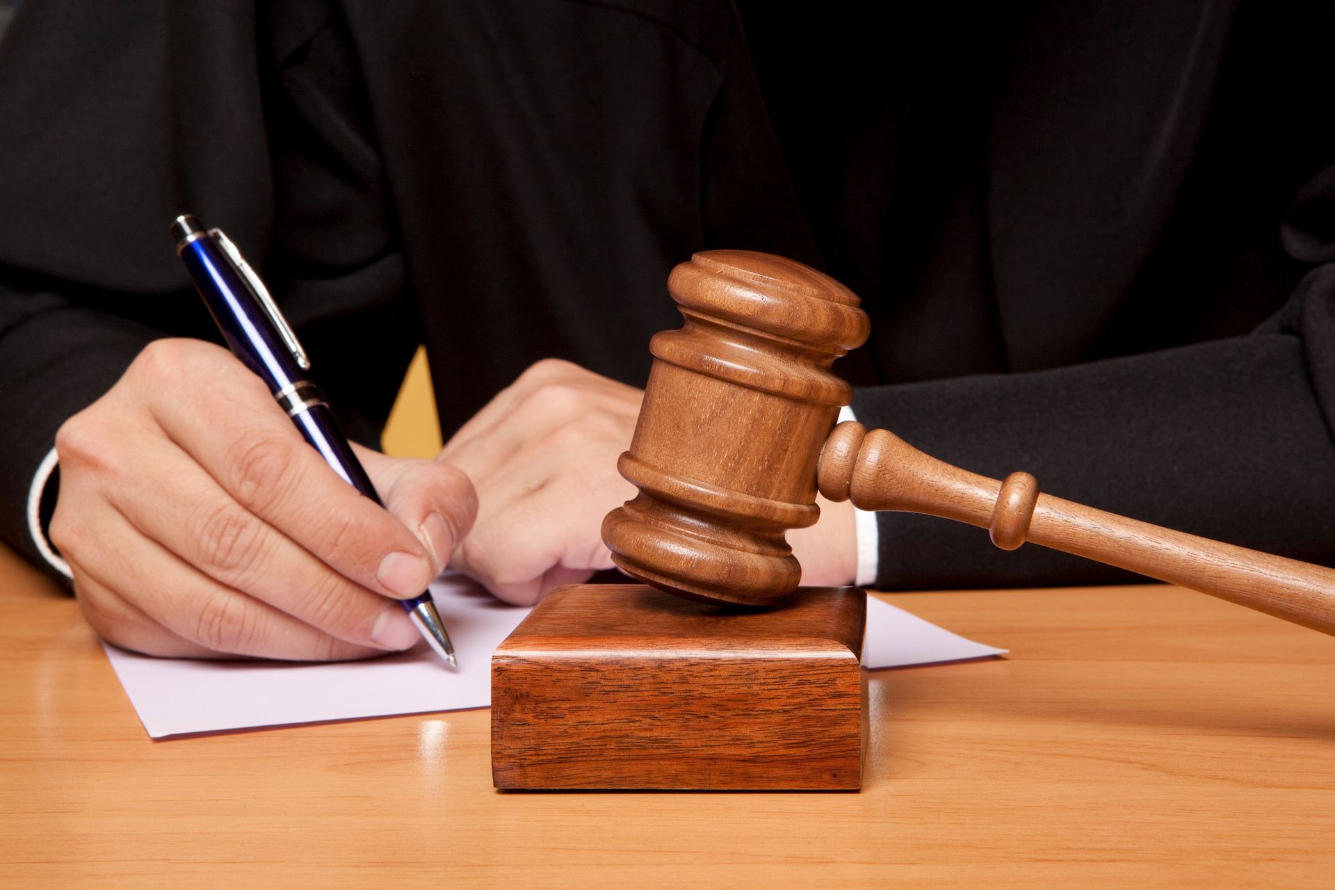 Judge writing on paper, gavel on wooden block on desk.
