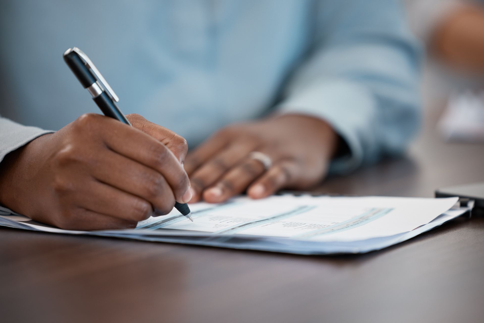 Person writing on paper with a pen at a table.