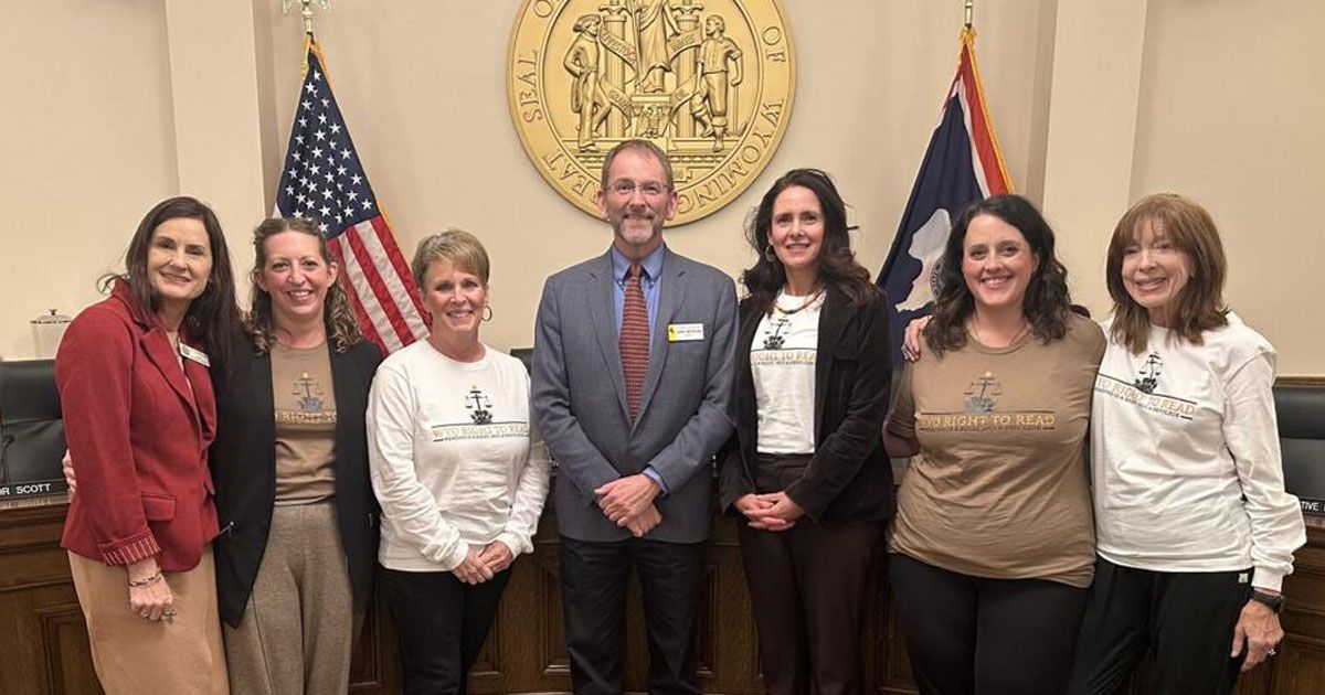 Group of people posing in front of flags and a seal in a government building.