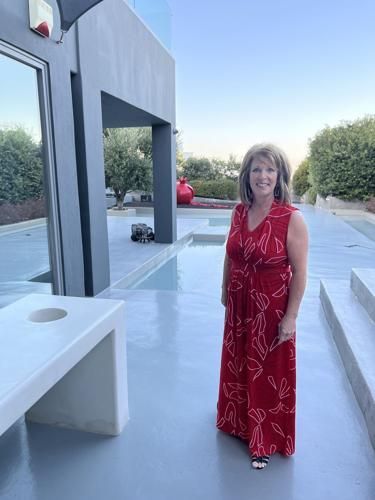 Woman in red dress stands outdoors near a modern building, gray patio, and small pool.