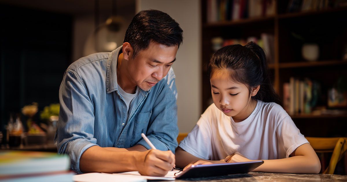 Man helping a child with homework, both looking at a tablet, writing, in a home setting.
