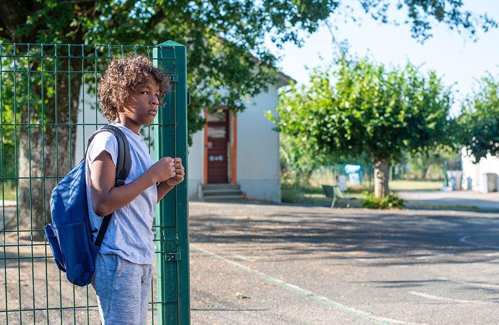 A person with a backpack stands by a green gate in front of a building.