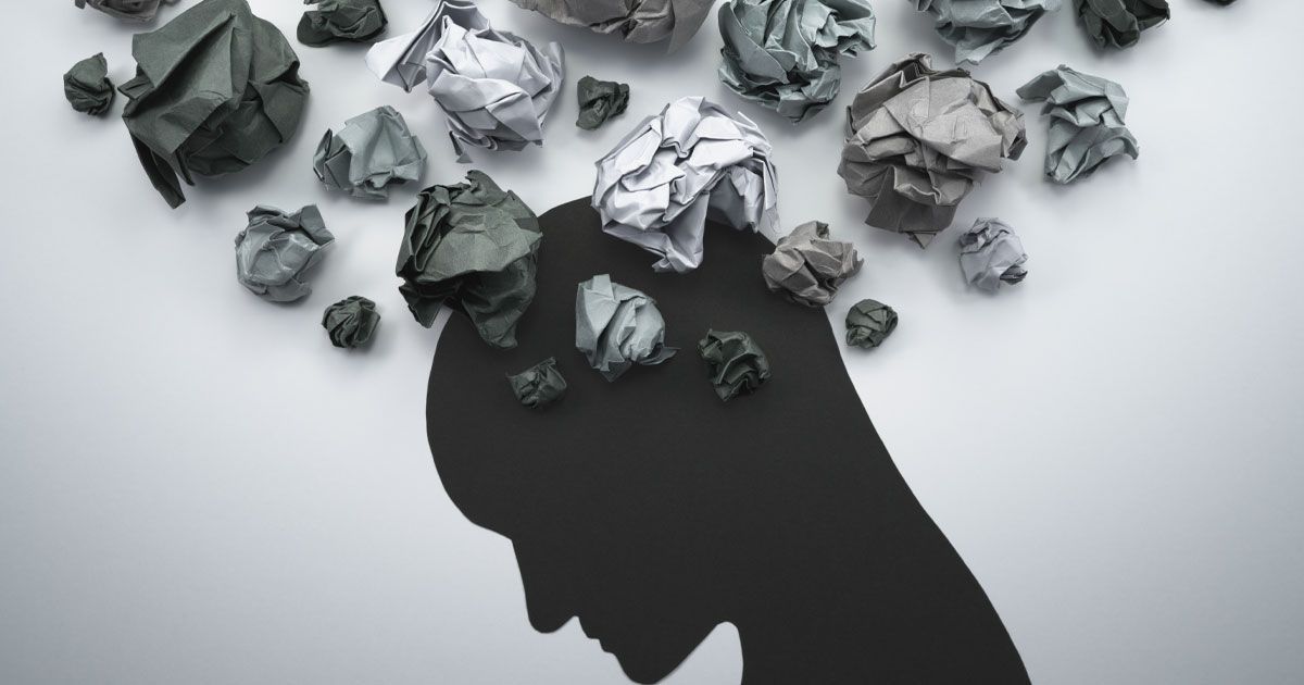 Silhouette of a head with crumpled paper balls above it, representing ideas and thoughts.