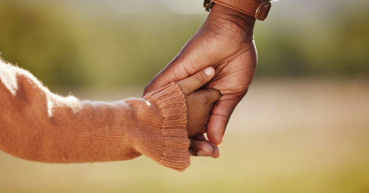 Adult hand holding a child's hand, outdoors. Warm tones.