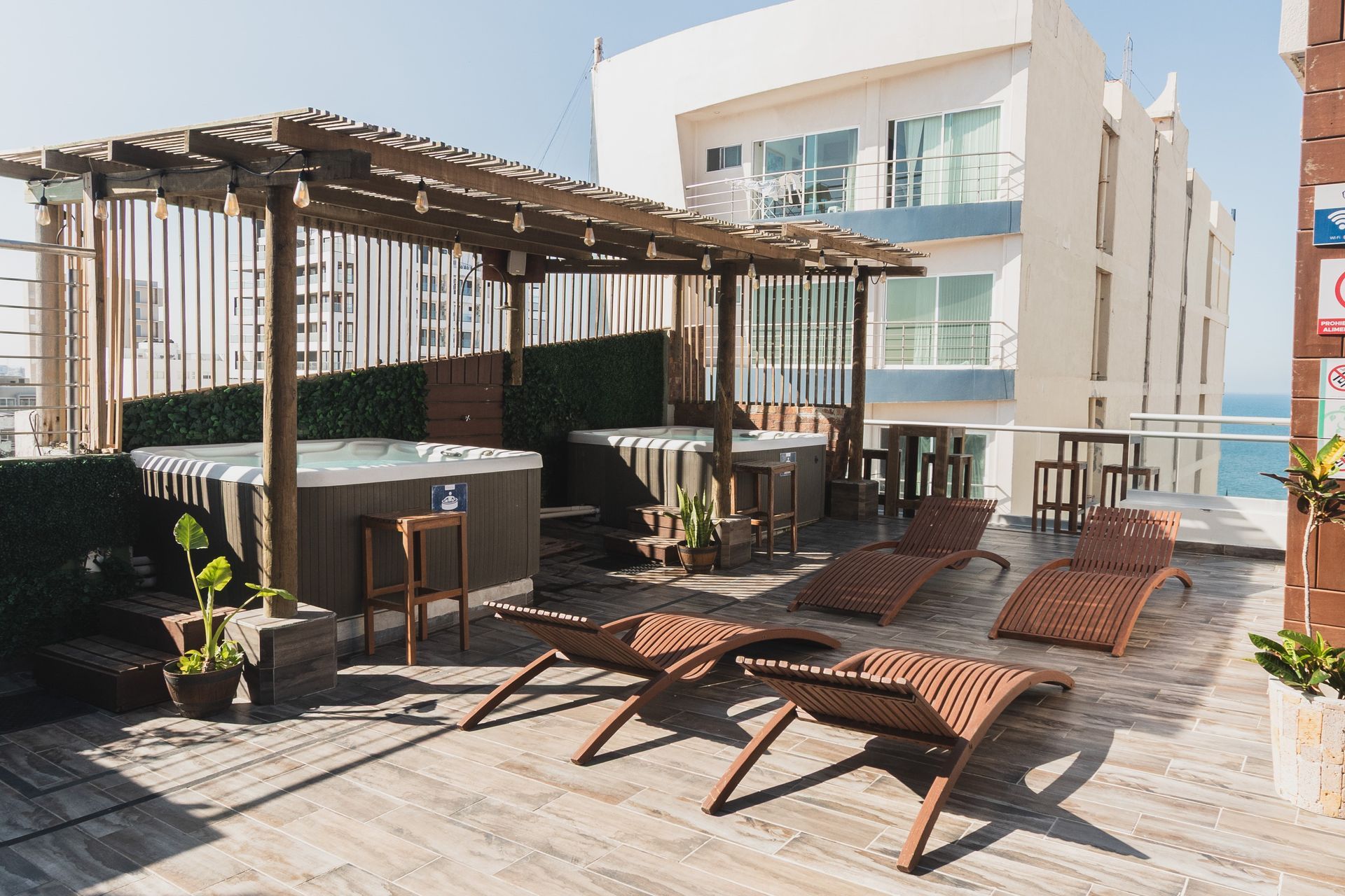 Un jacuzzi en una azotea con una piscina al fondo.