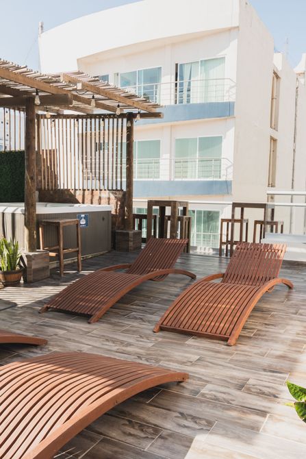 Una terraza en la azotea con tumbonas de mimbre marrón sobre una tarima de baldosas, junto a una pérgola de madera y un jacuzzi.