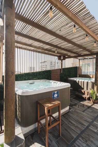 Dos jacuzzis exteriores en una terraza de madera con luces de guirnalda, junto a un taburete alto de madera.