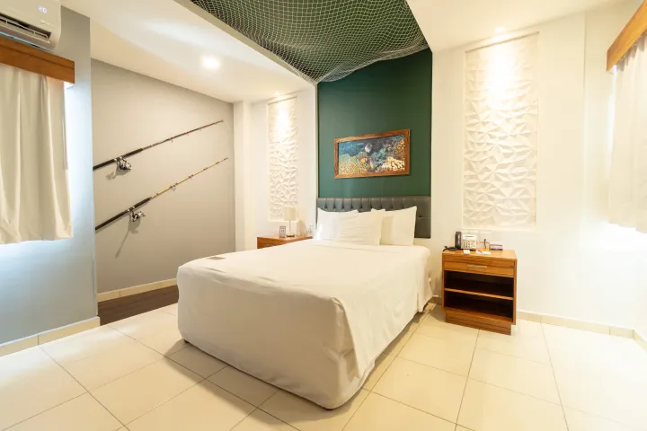 Un dormitorio con una cama blanca central, una pared decorativa de color verde, un diseño ornamentado en el techo y dos cañas de pescar montadas en la pared.