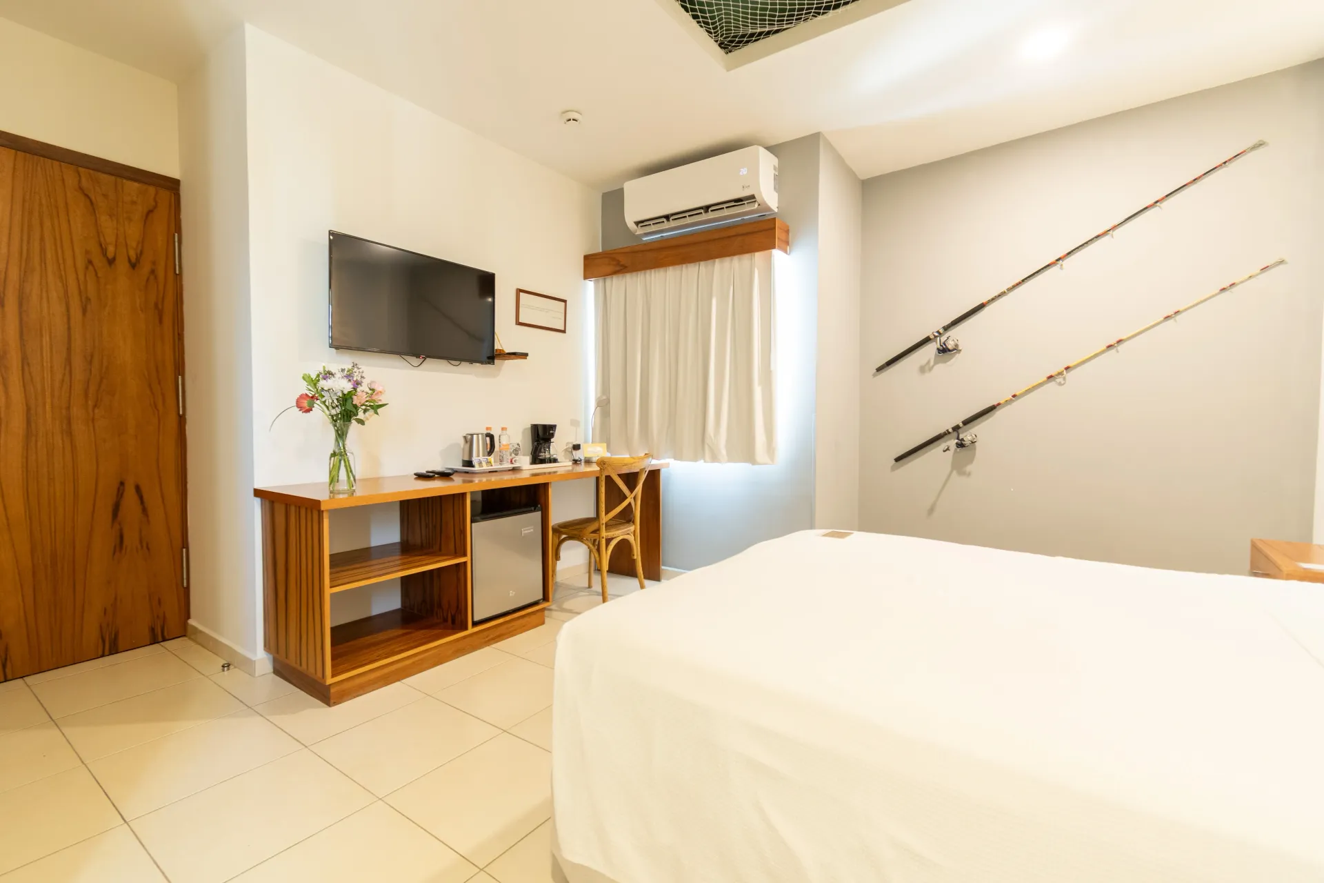 Una habitación de hotel con una cama, un televisor sobre una repisa de madera, un escritorio con una silla y dos cañas de pescar colgadas en la pared.