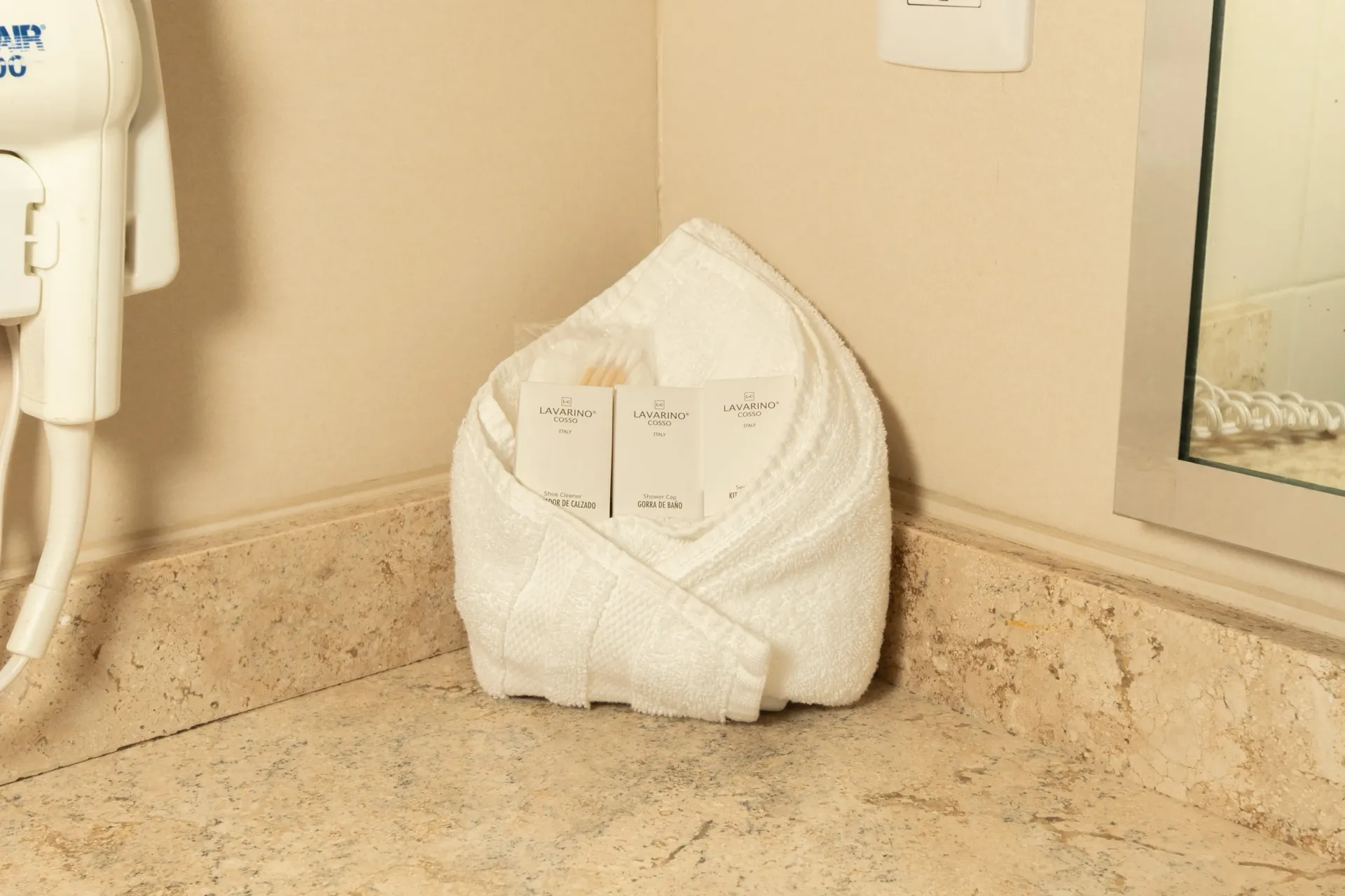 Una toalla blanca doblada sostiene pequeños frascos de artículos de tocador sobre una encimera de baño de piedra beige.