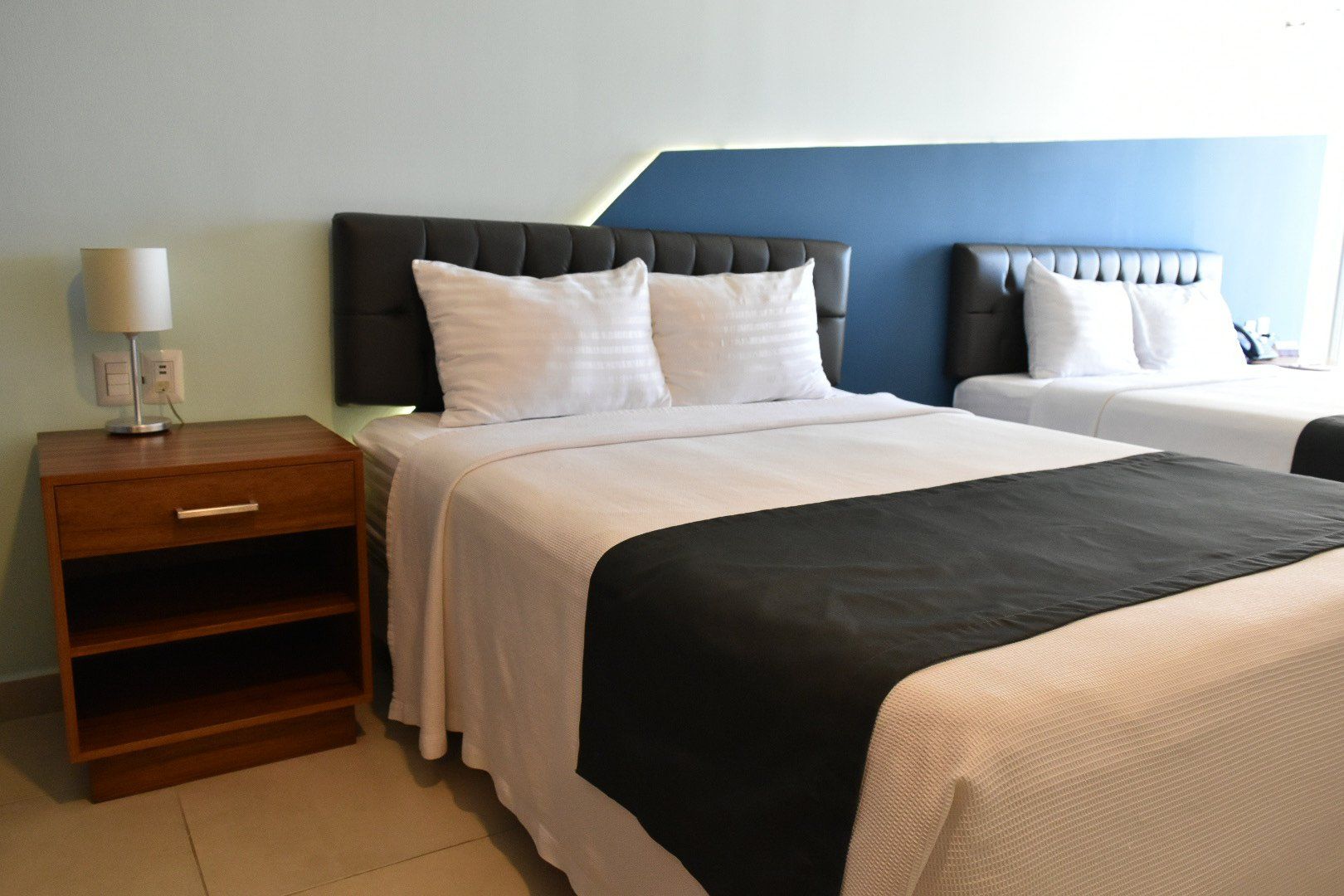 A hotel room with two beds , a nightstand and a lamp.