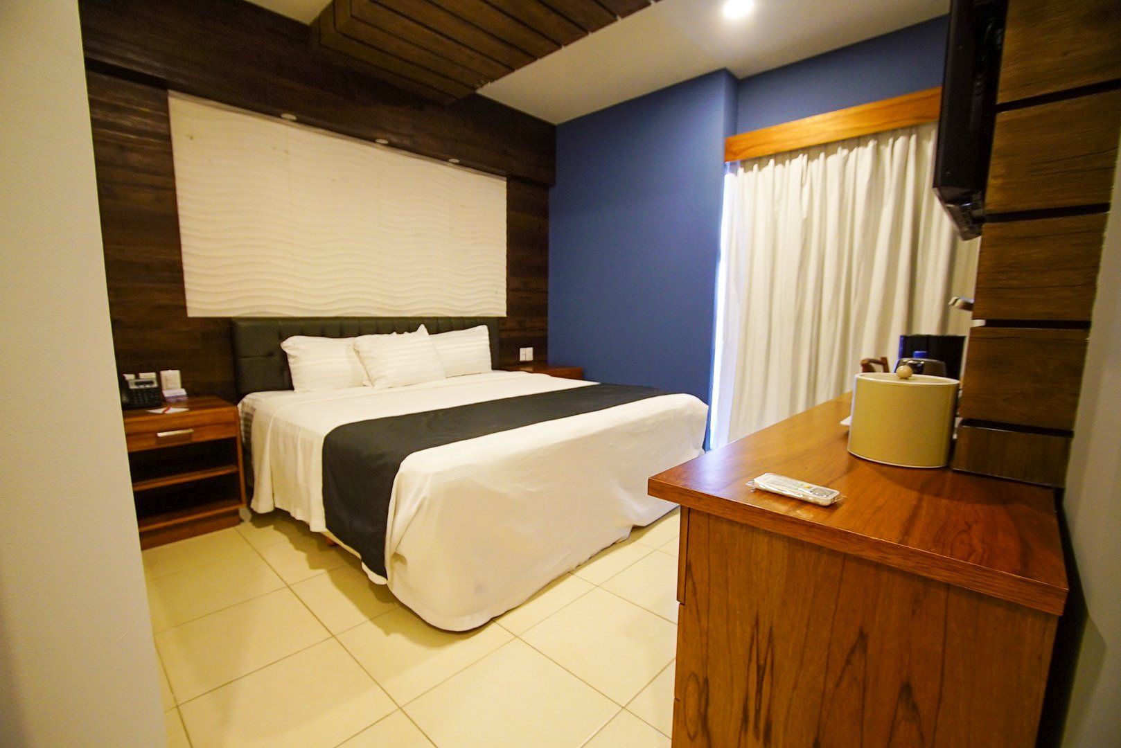 A hotel room with a king size bed and a wooden dresser.