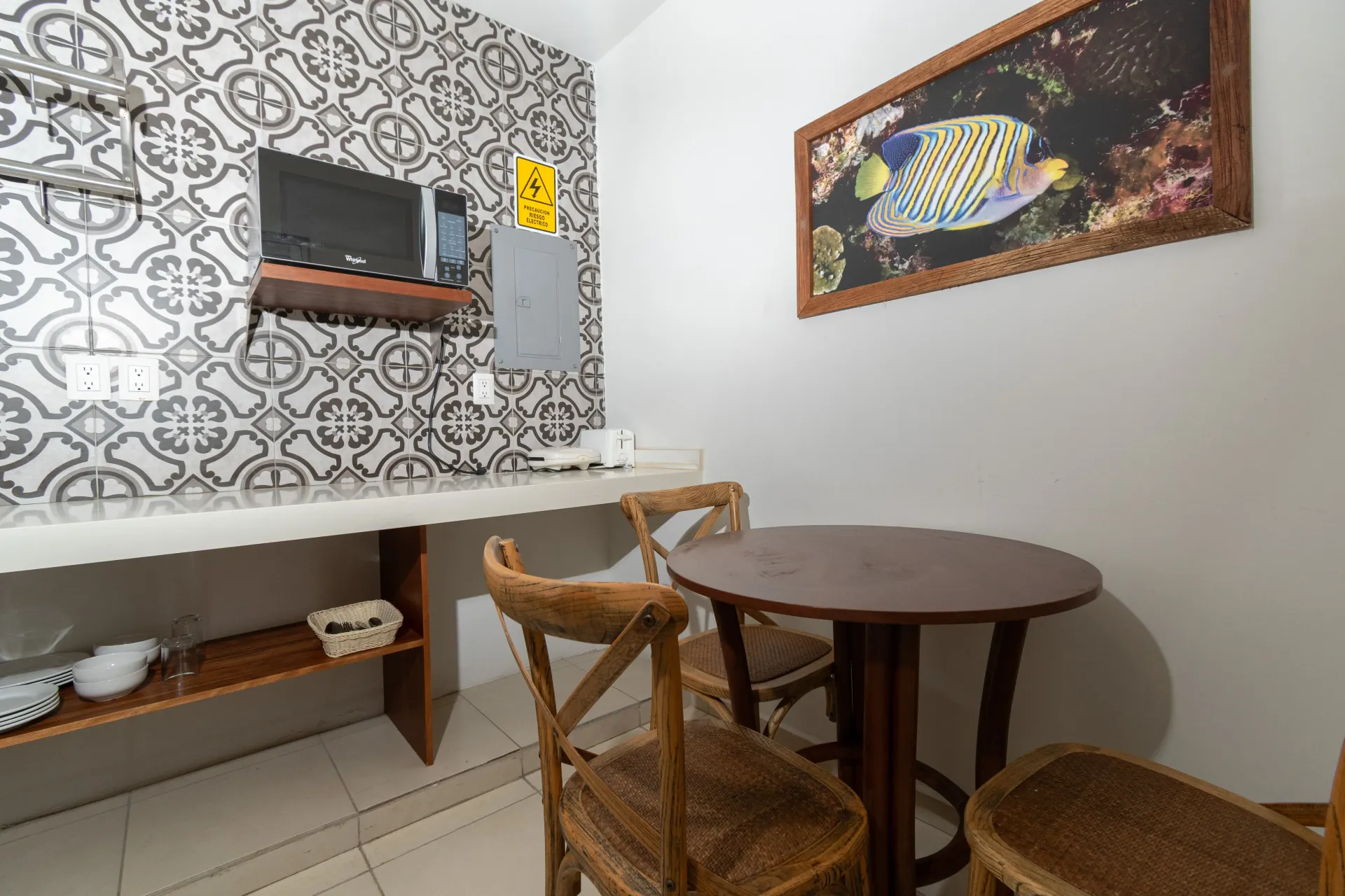 Una zona de cocina con azulejos decorativos en la pared, un microondas, una encimera, una pequeña mesa redonda de madera y tres sillas de madera.