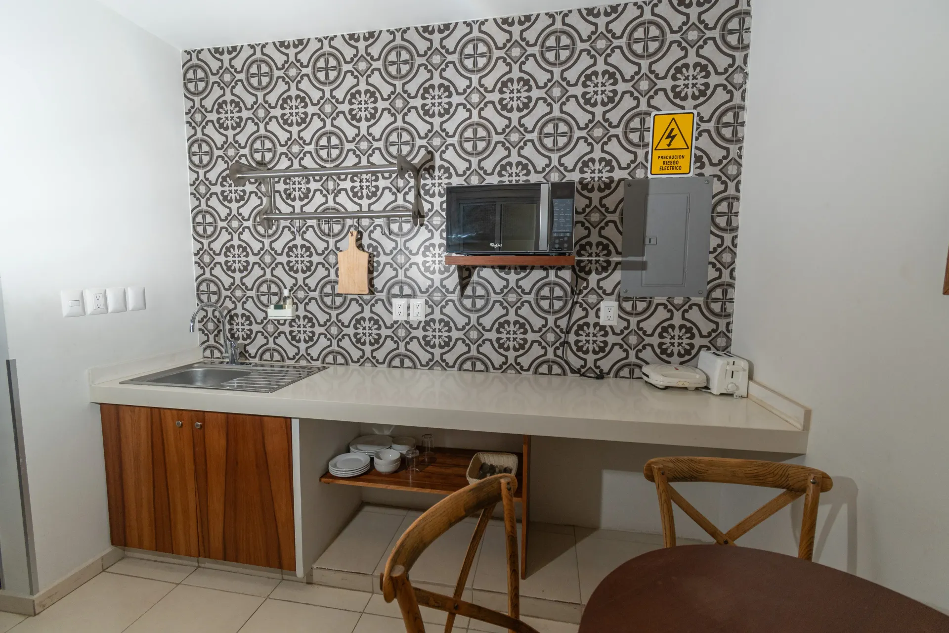 Una pequeña zona de cocina con paredes de azulejos estampados, una encimera de hormigón, armarios bajos de madera y un microondas.