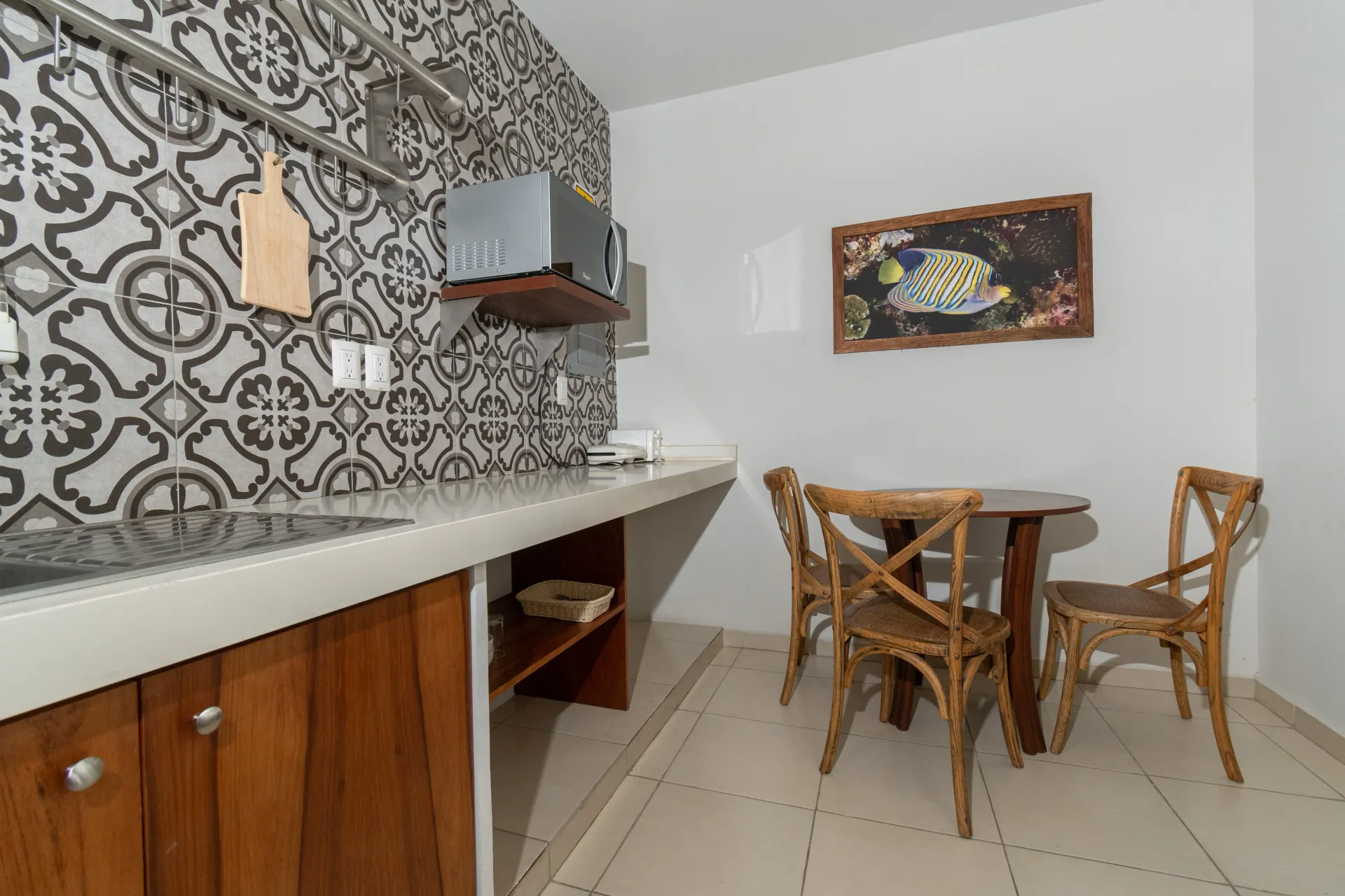 Una cocina con un salpicadero de azulejos estampados, armarios de madera, un microondas y una pequeña mesa de comedor con dos sillas.