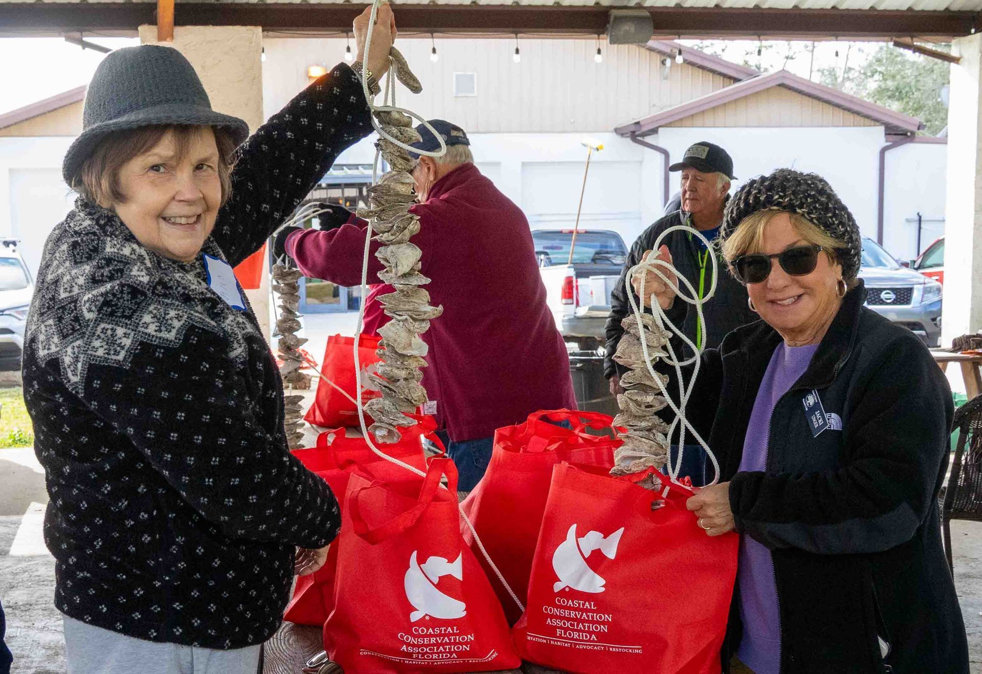 Two women are standing next to each other holding red bags.