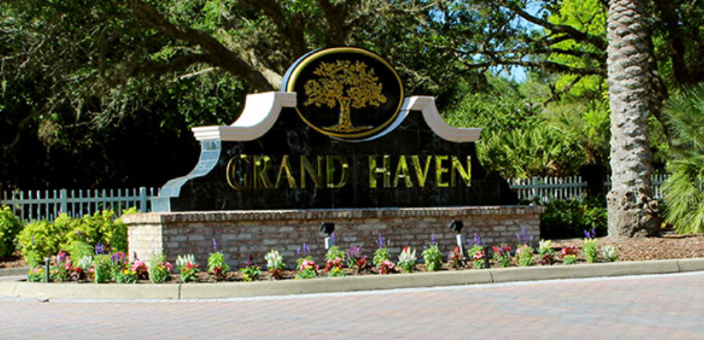 A sign for grand haven is sitting on the side of the road.