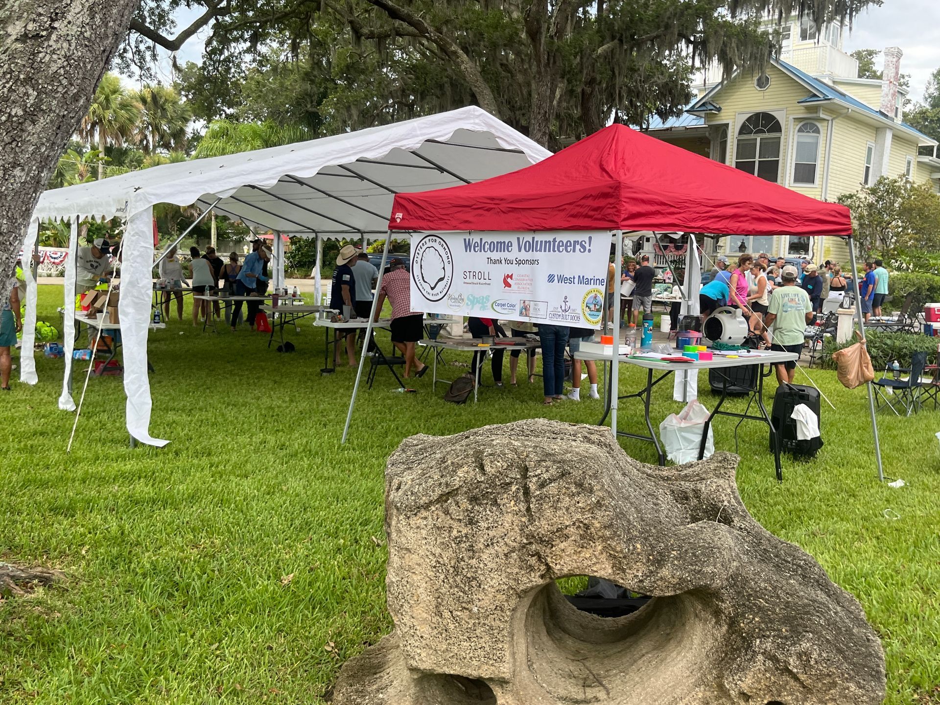 A group of people are sitting under a tent in a grassy field.