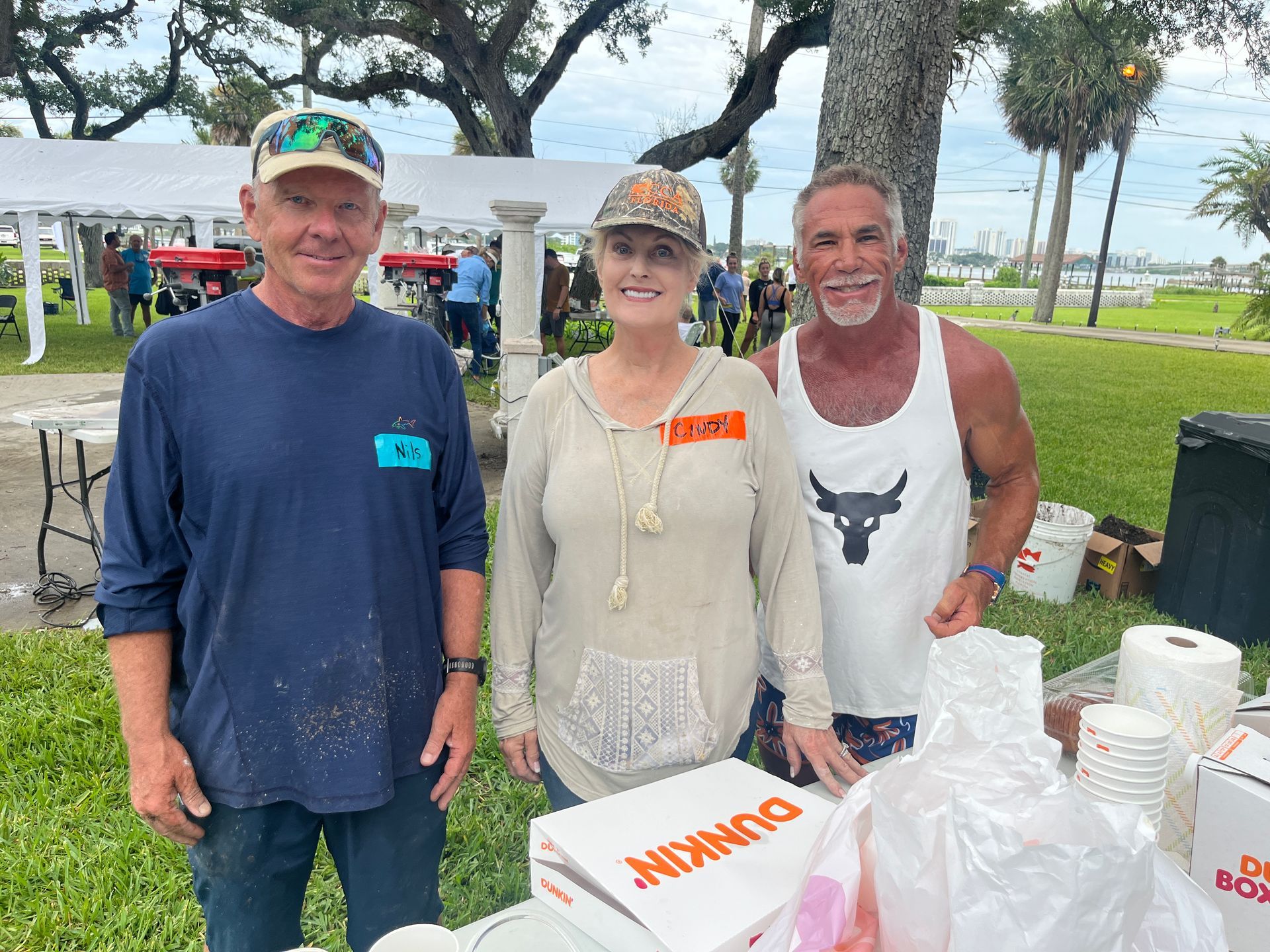 Three people are posing for a picture in front of a dunkin donuts box.