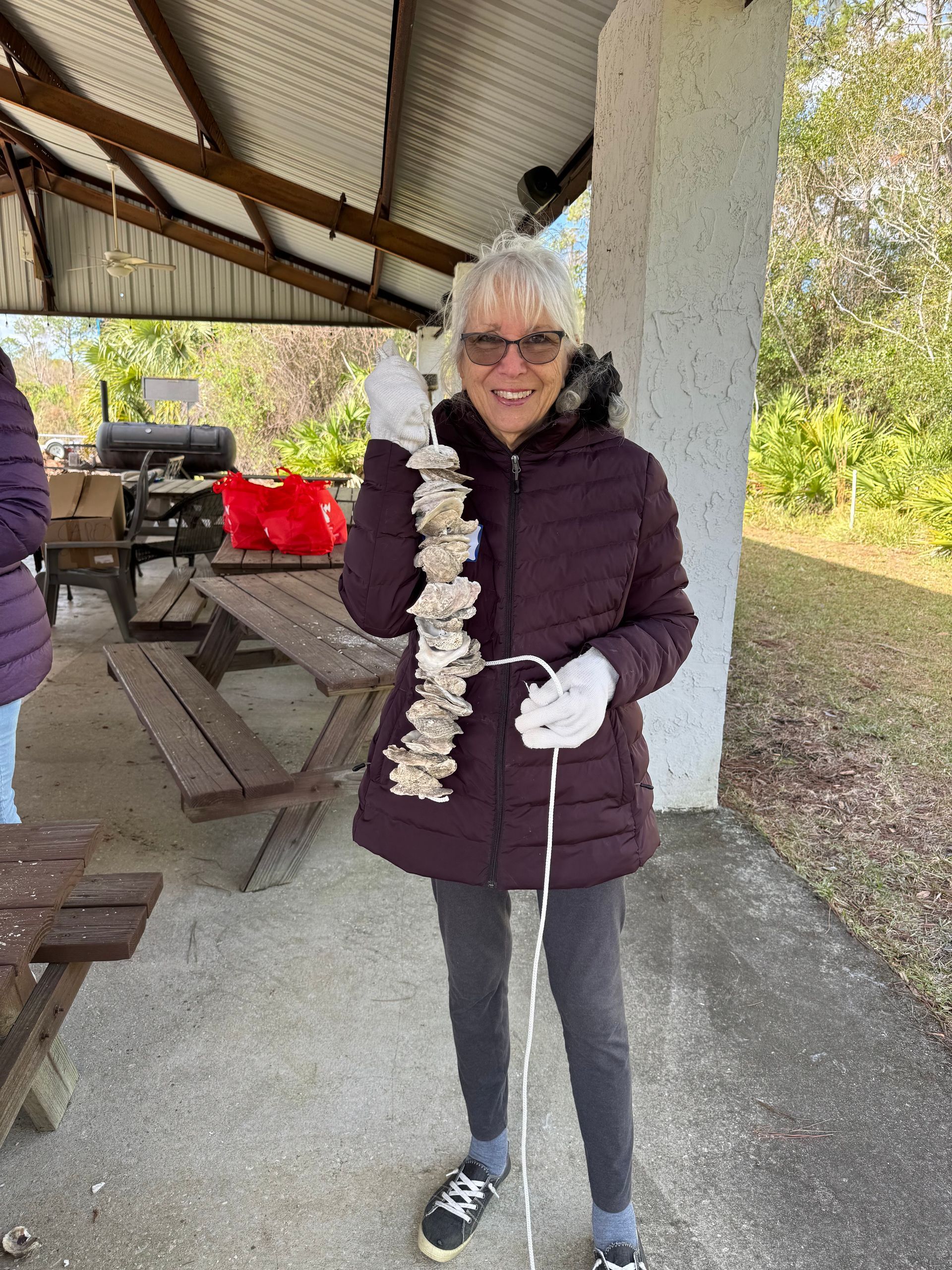 A woman in a purple jacket is holding a string of oysters.