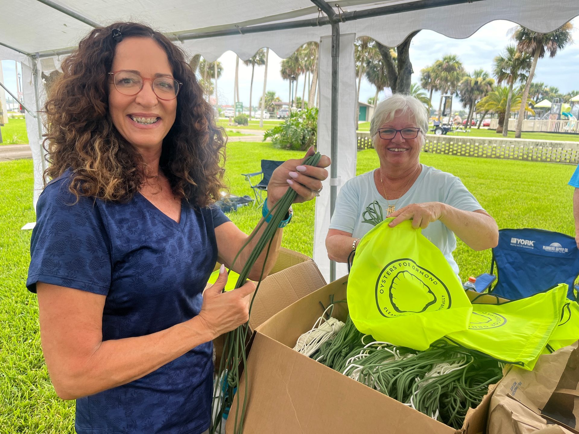 Two women are standing next to each other under a tent holding a box of flowers.