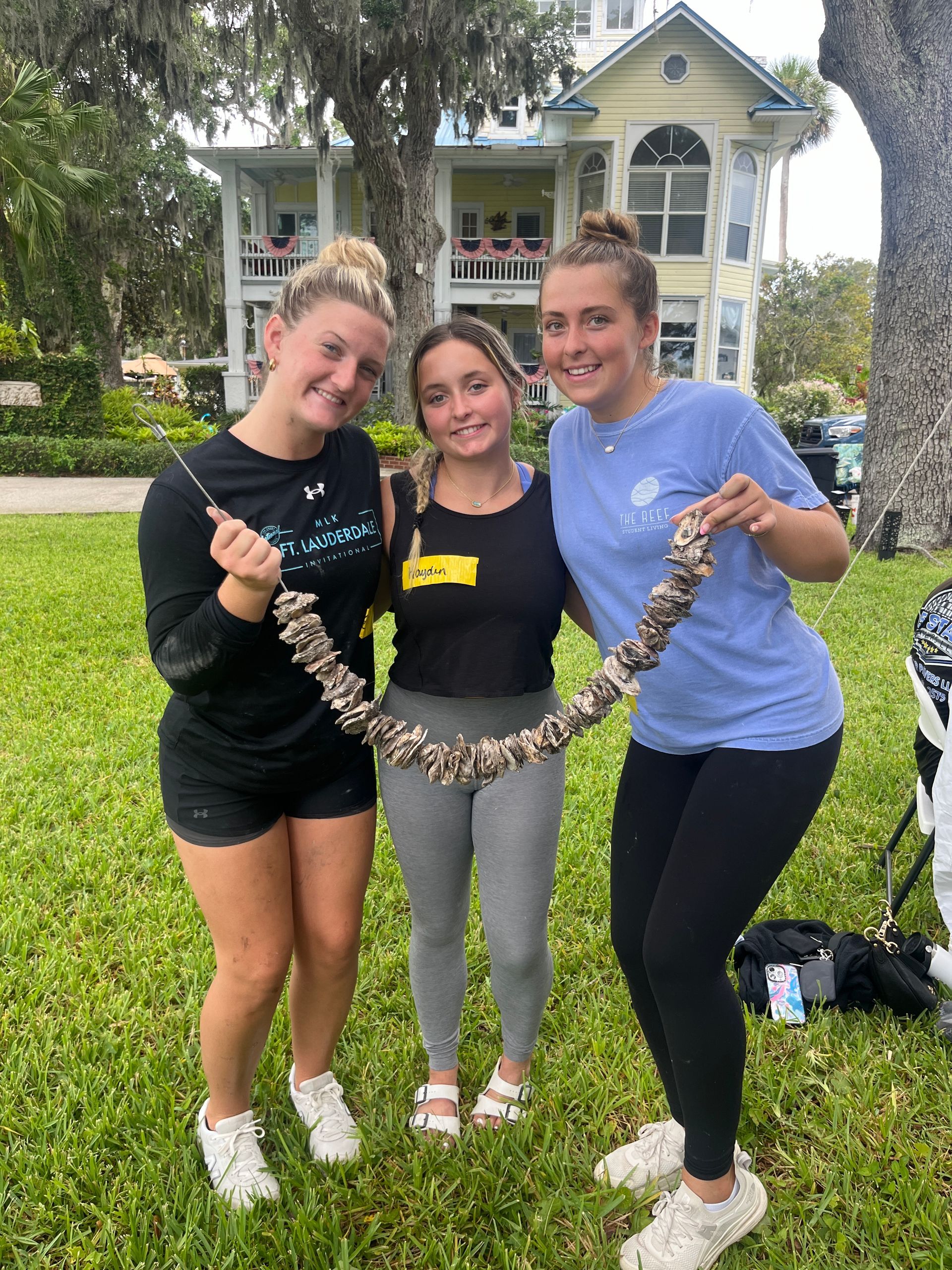 Three young women are standing in the grass holding oysters.