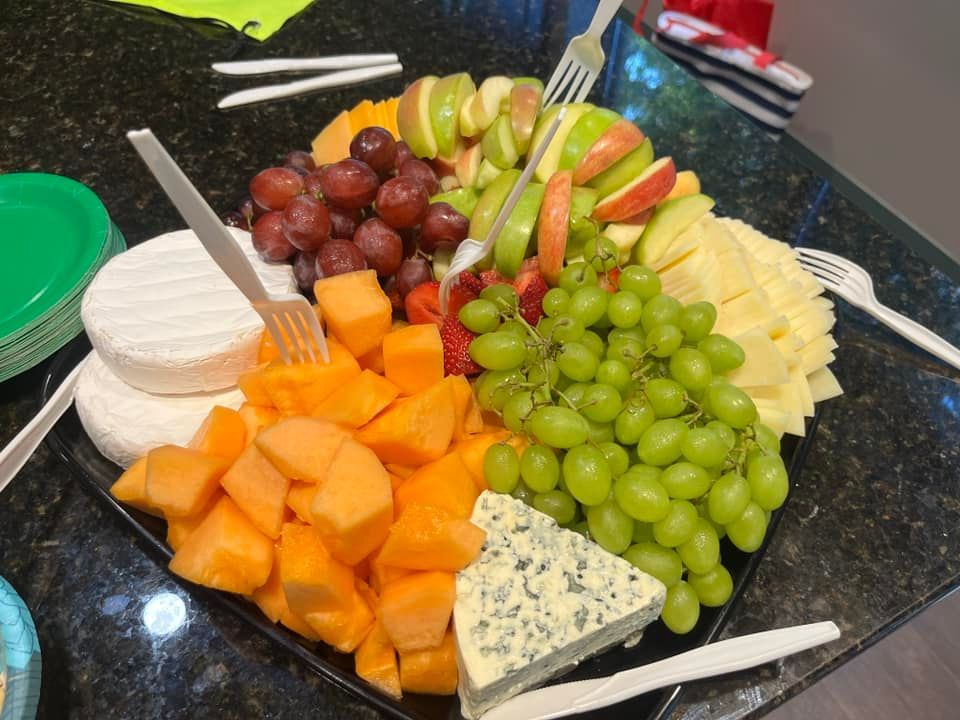 A plate of fruit and cheese on a table with knives and forks