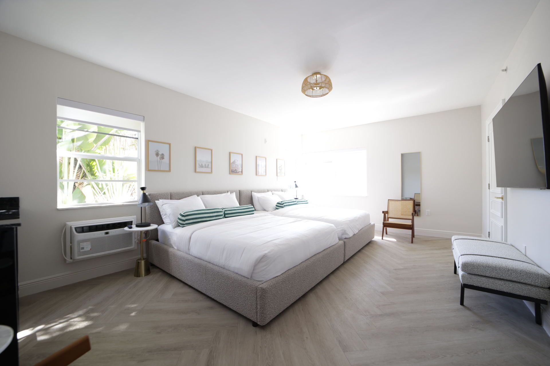 Spacious bedroom with two queen beds, a window, and a TV. Light-colored walls and wood flooring.
