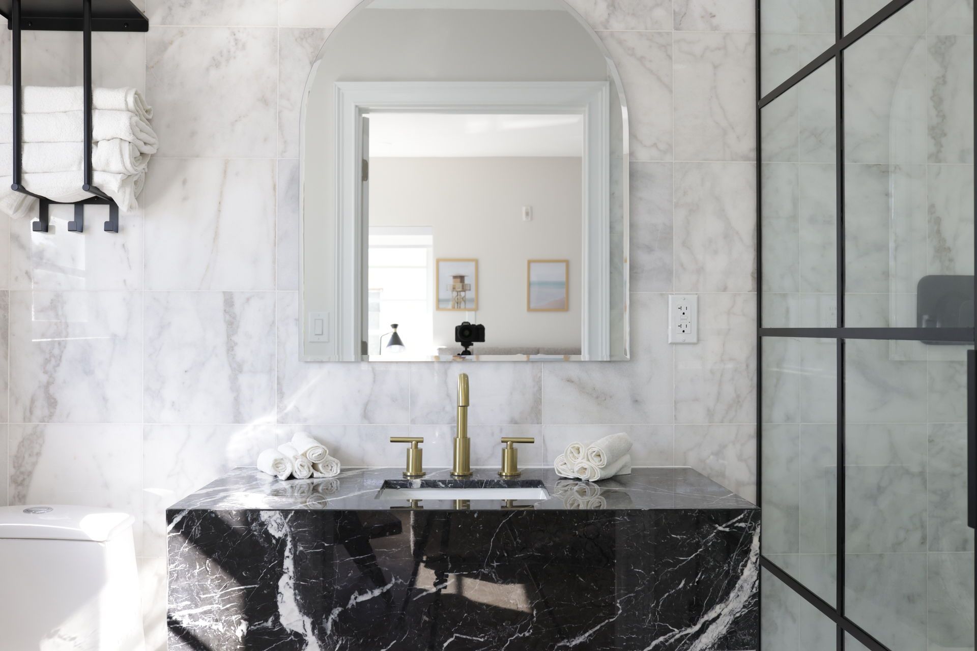 Bathroom with marble walls and a black marble vanity, gold fixtures, and an arched mirror.