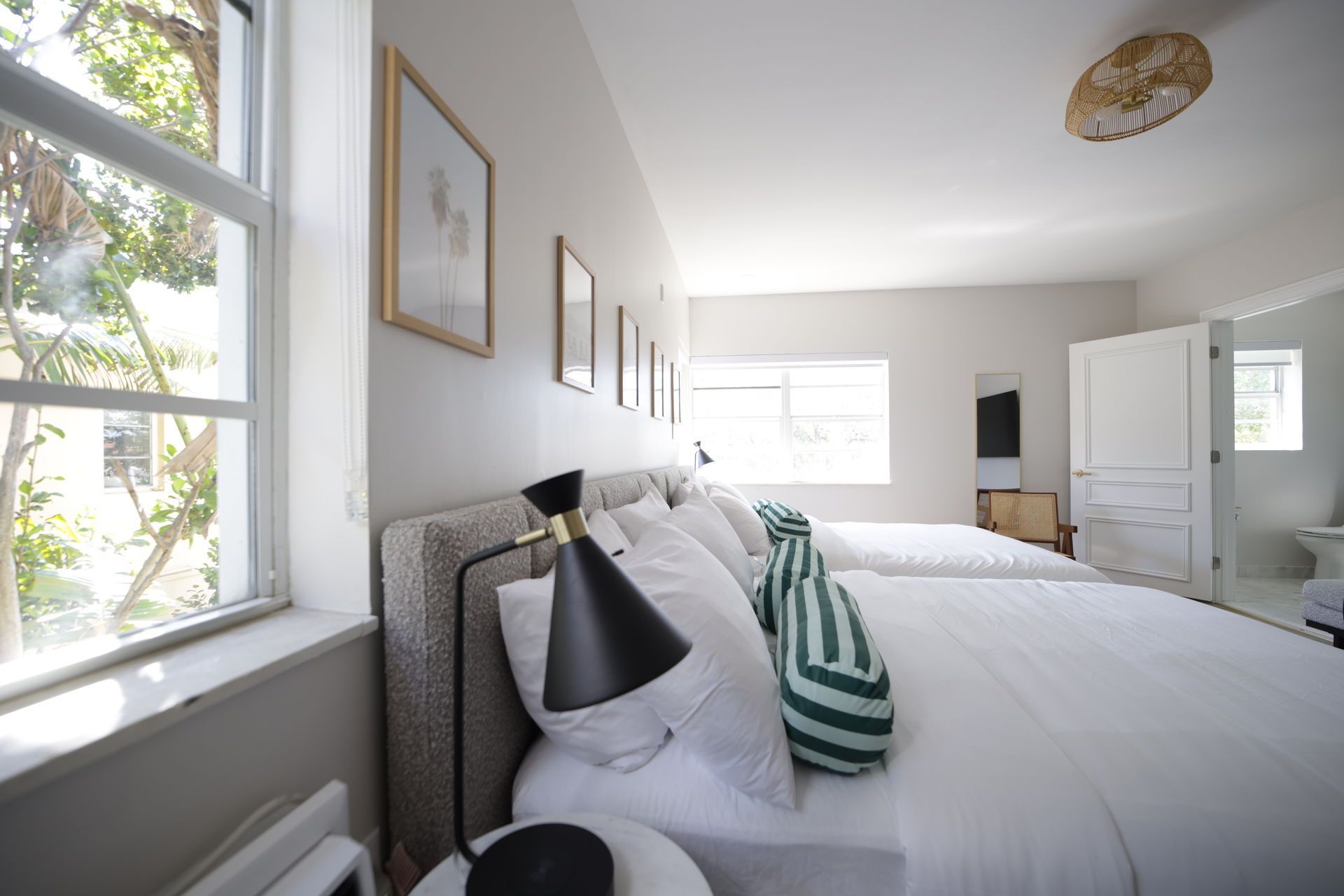 Bedroom with two beds, white linens, large window, framed art, and a lamp.