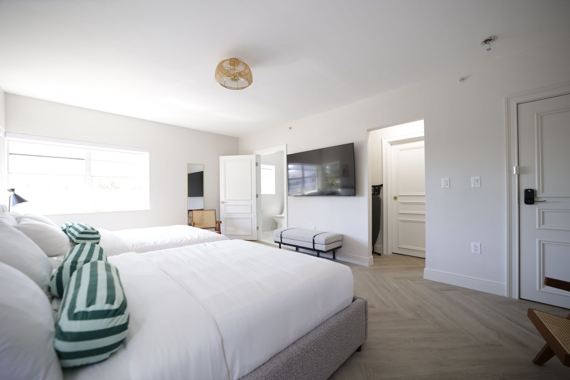 A bright bedroom with two beds, a TV, and a door to a bathroom.