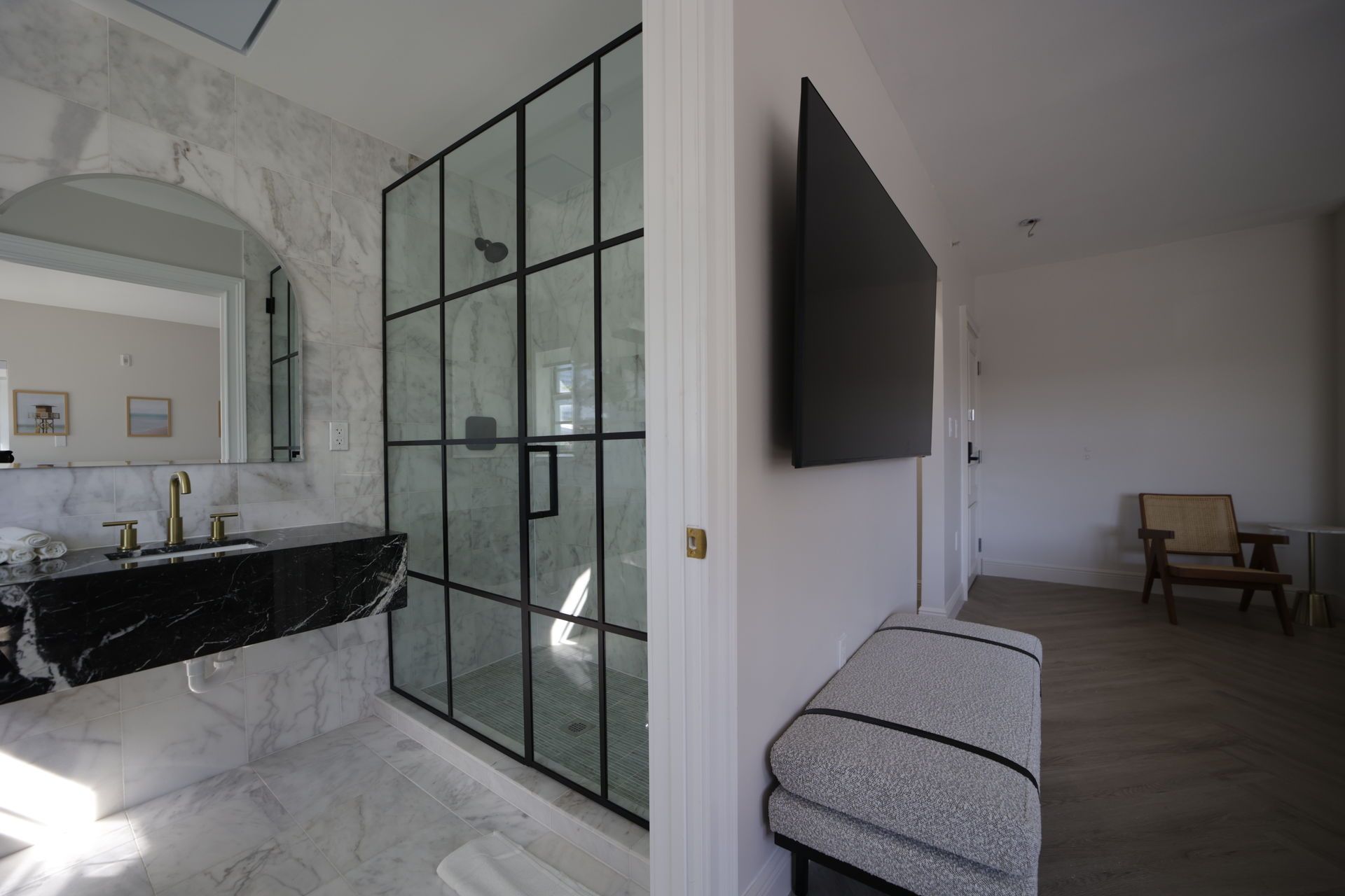 Modern bathroom with a glass shower, black vanity, and a TV on the wall.