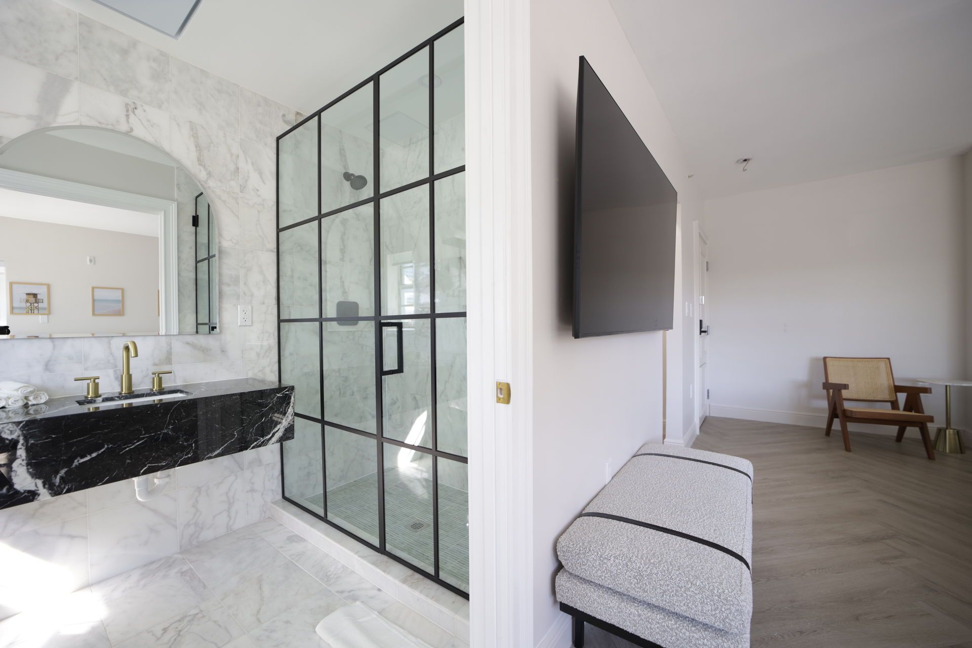 Modern bathroom with black framed shower, marble vanity, and TV.