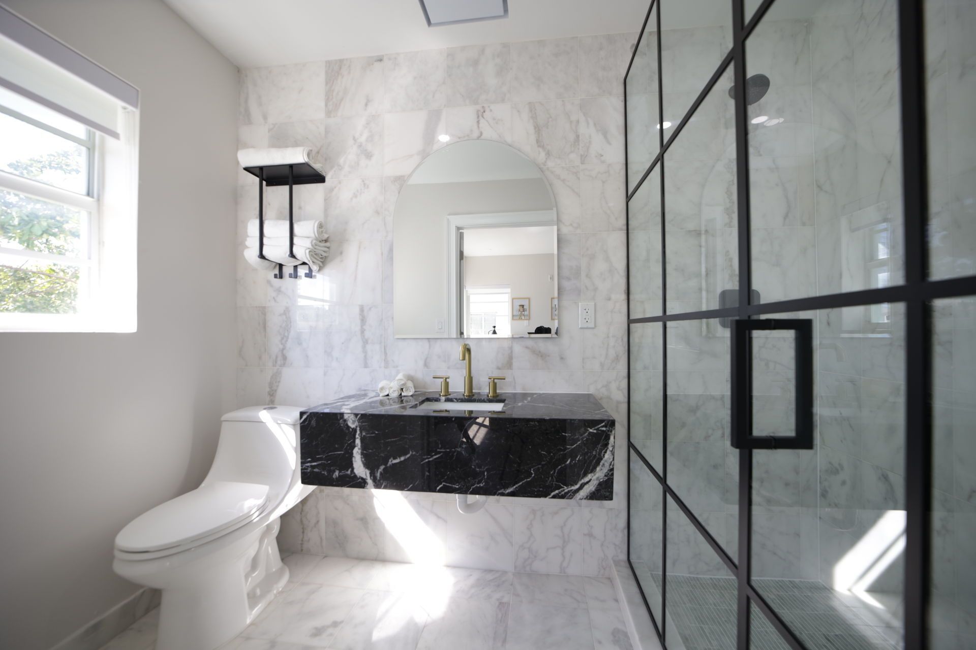 Modern bathroom with marble walls, black vanity, large shower, and toilet.