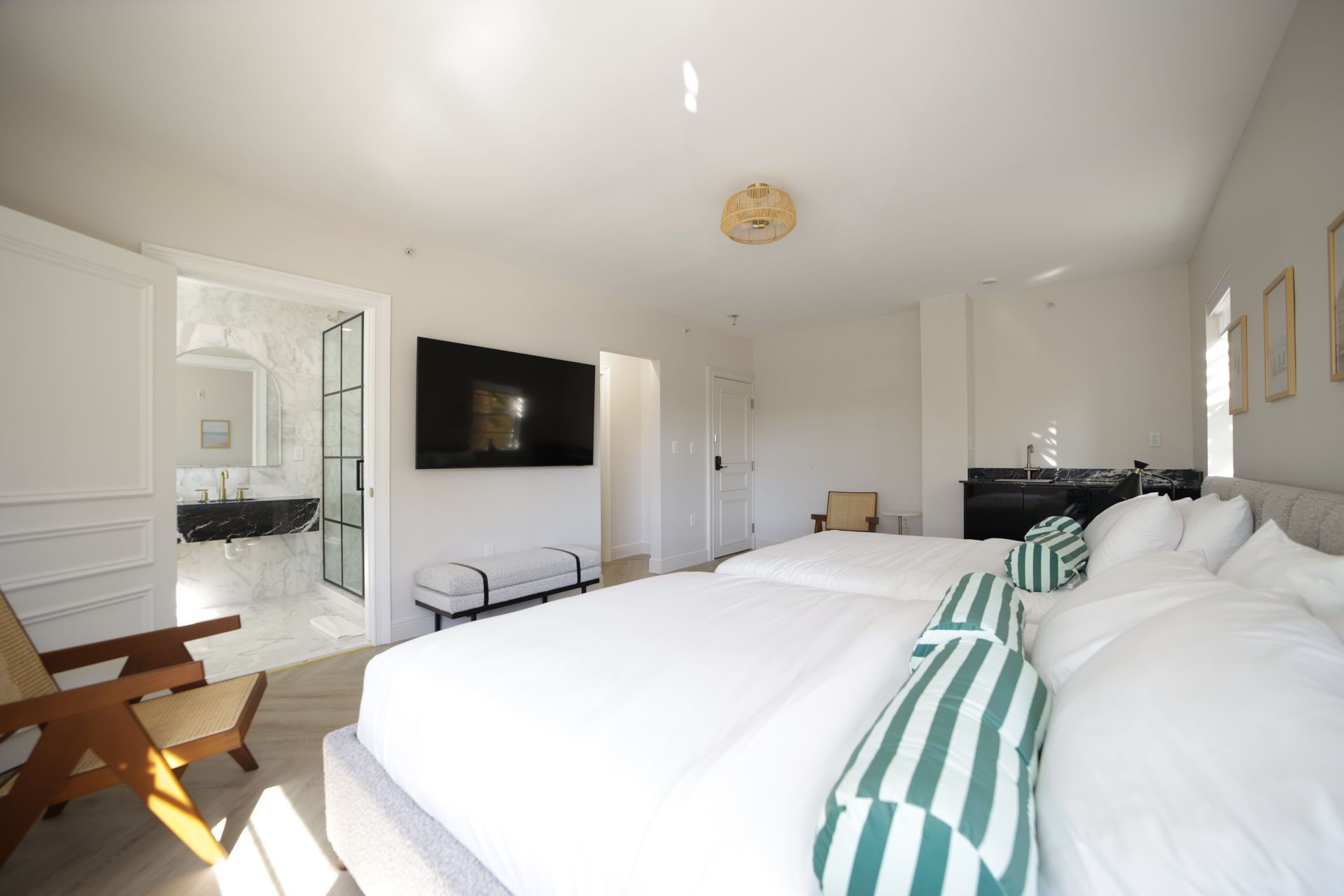 Bright bedroom with two beds, open to a bathroom, and a mounted TV.