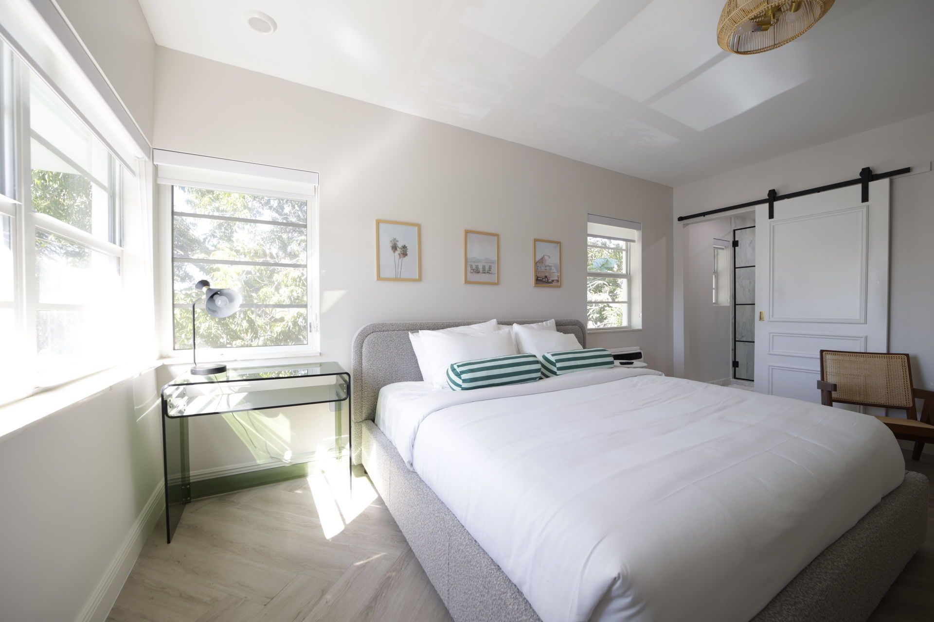 Bedroom with large windows, a bed with white bedding, and a sliding barn door.