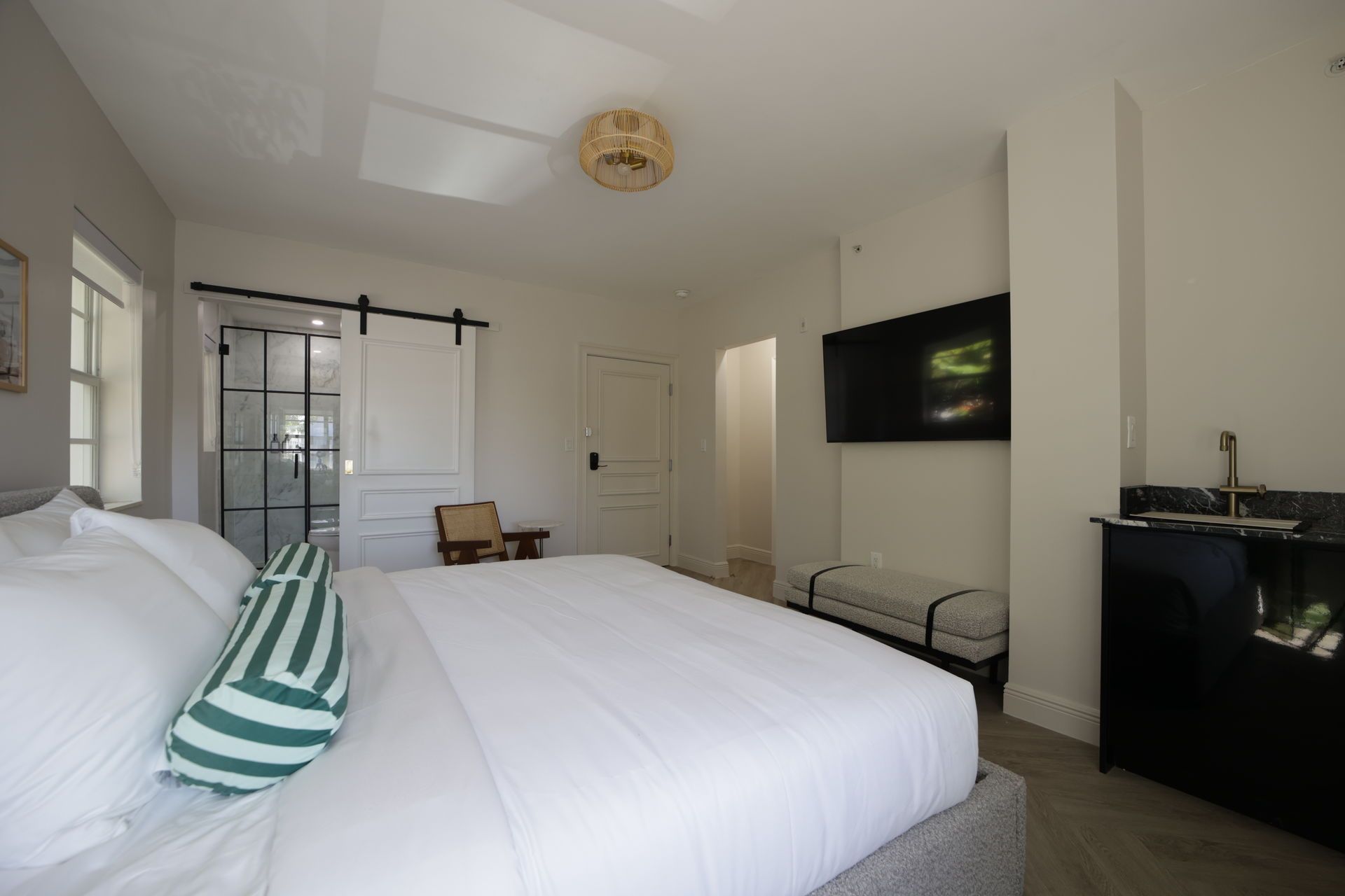 Bedroom with a large bed, TV, and black bar area. A sliding glass door leads to a shower.