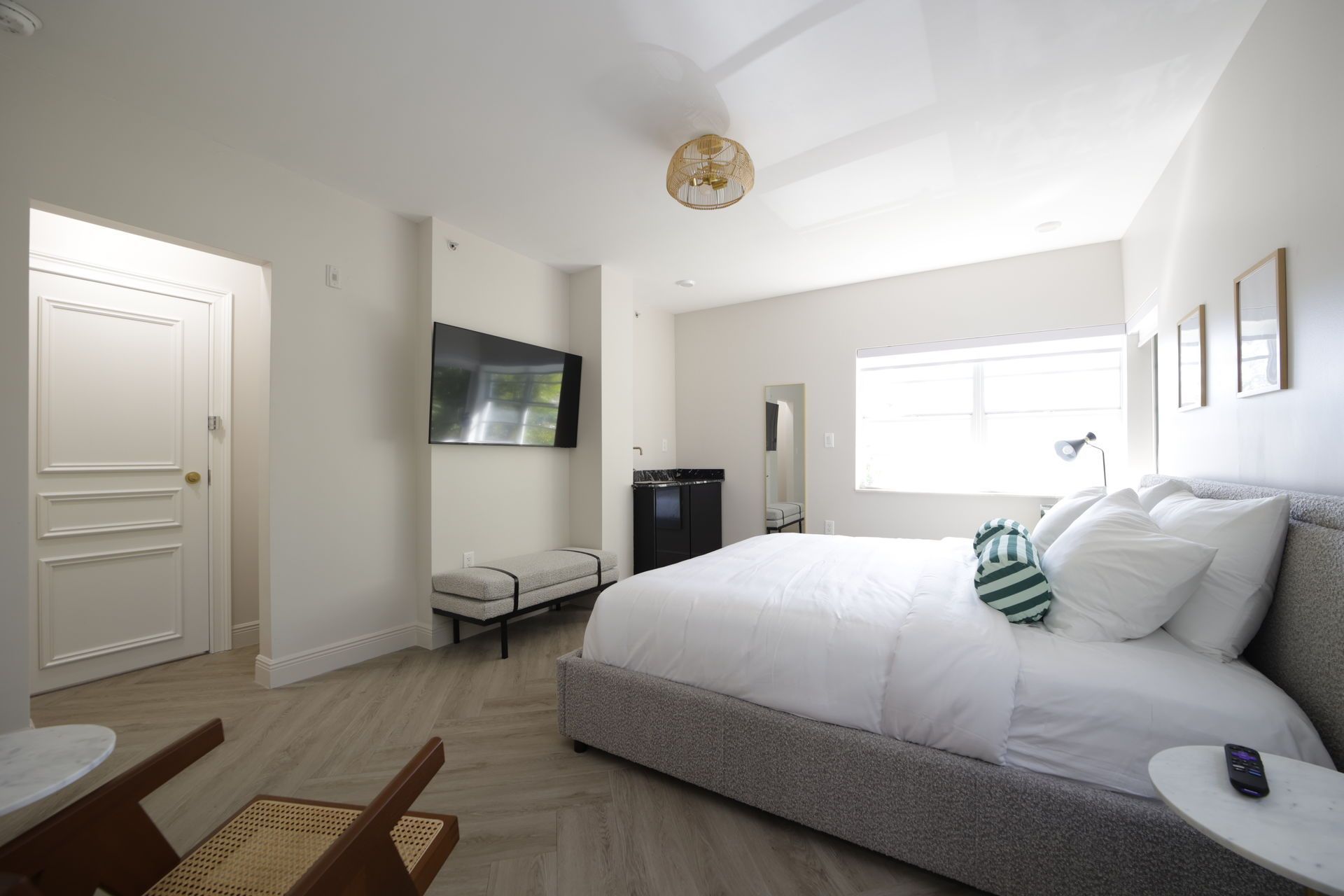 Bright hotel room with king-size bed, TV, mini-fridge, and large window.