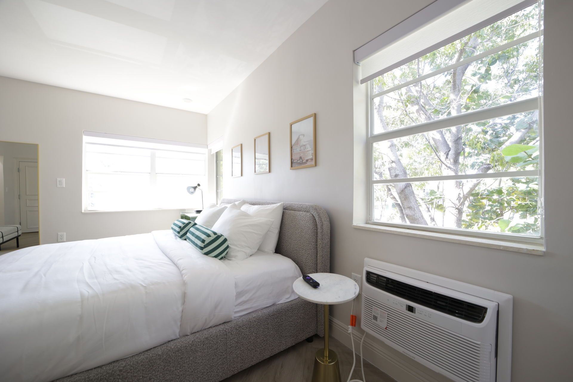 Bedroom with a bed, two windows, and framed art on the wall. An air conditioner is mounted below a window.