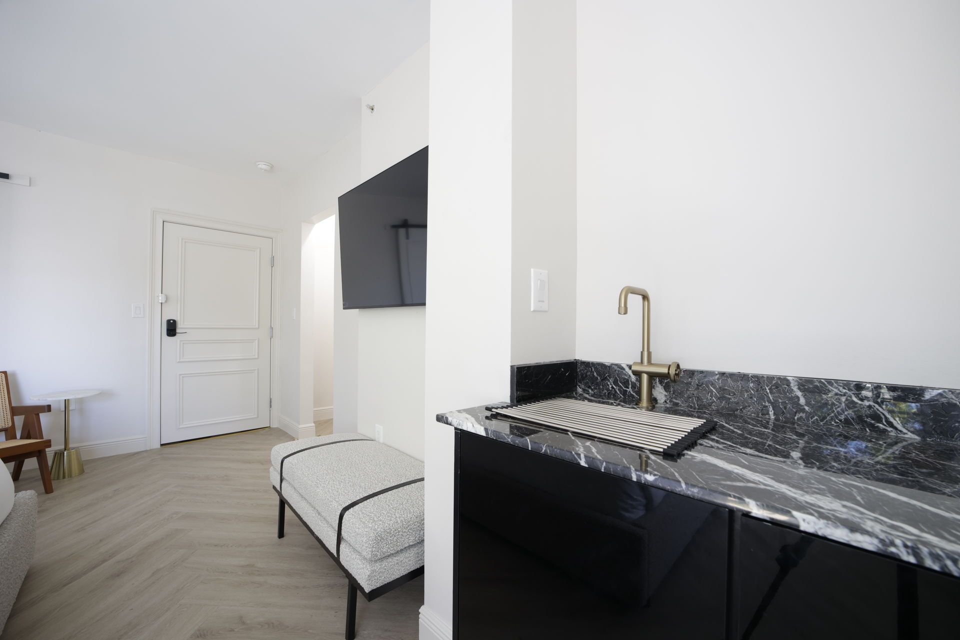 Interior view of a room with a TV, a bench, and a sink on a black marble countertop.
