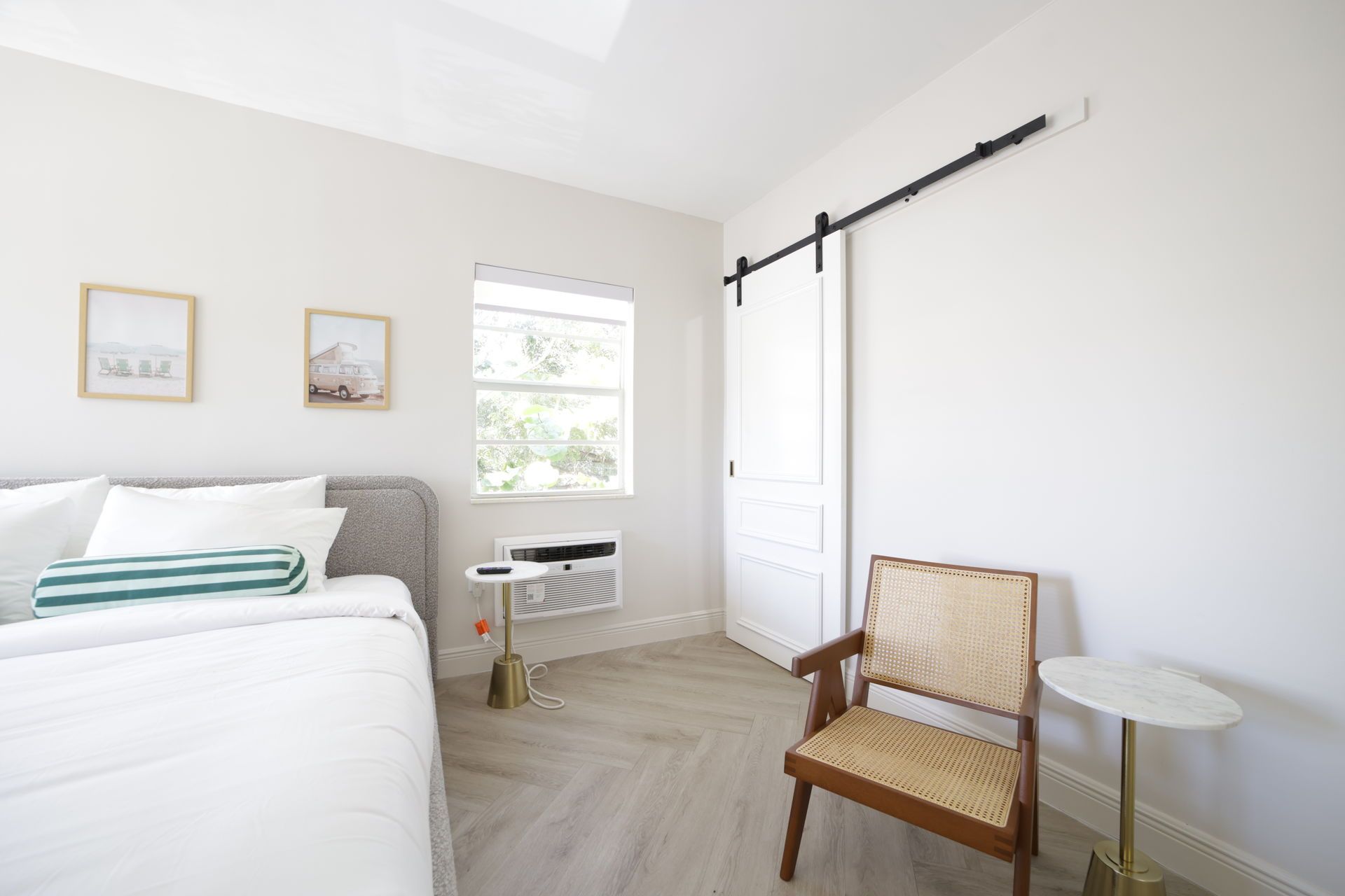 Bedroom with a bed, sliding door, chair, small table, window, and wall art; light tones.