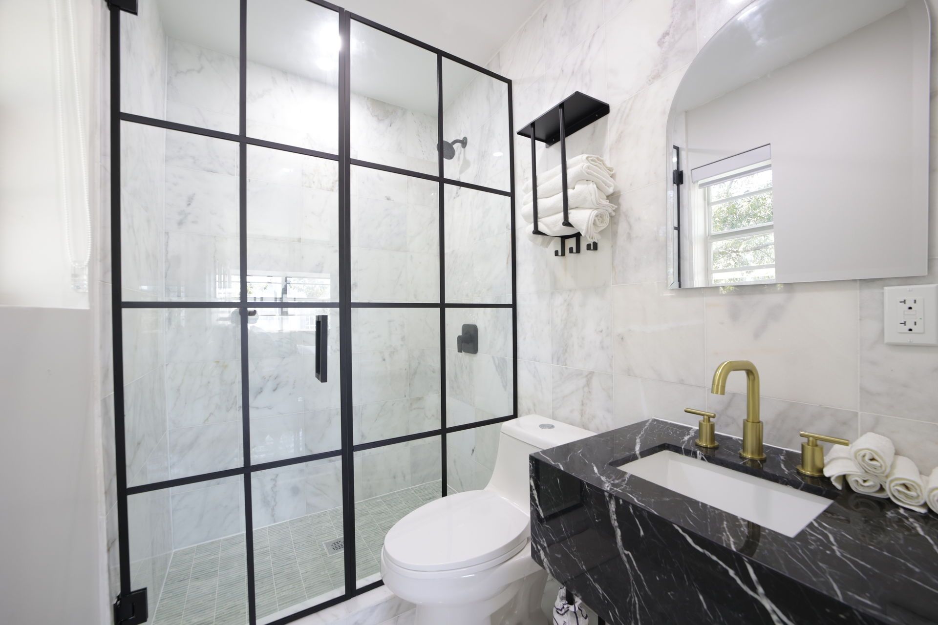 Modern bathroom with black framed shower, black marble vanity, and gold faucet.