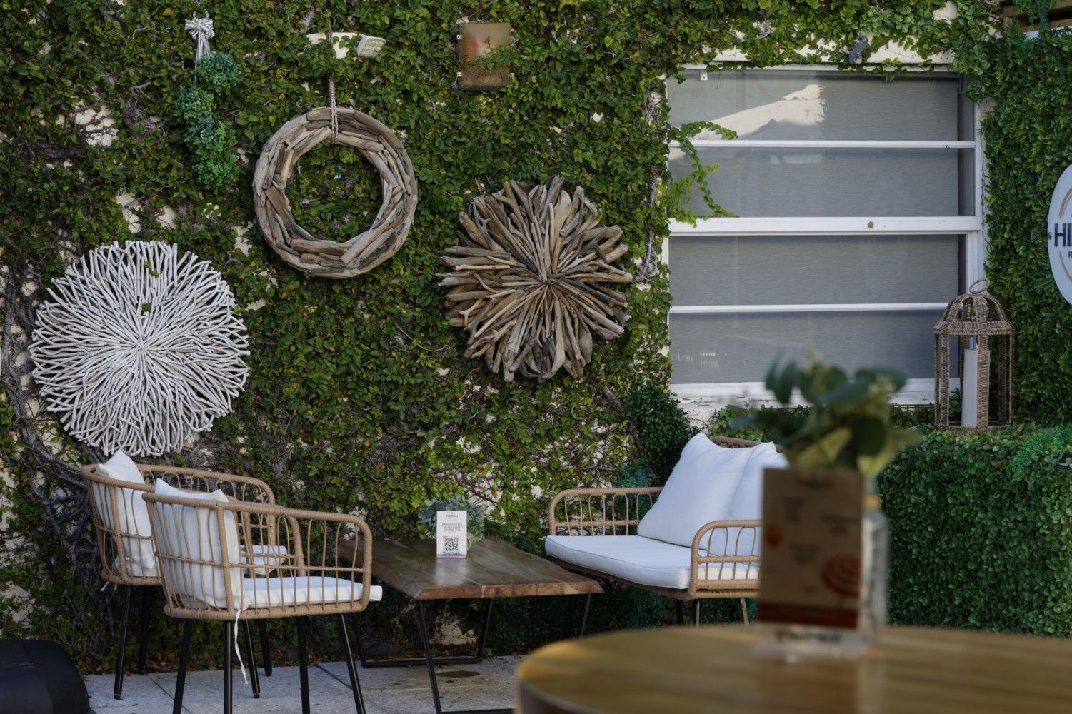 Outdoor seating area with ivy-covered wall, decorative wreaths, and wicker furniture.