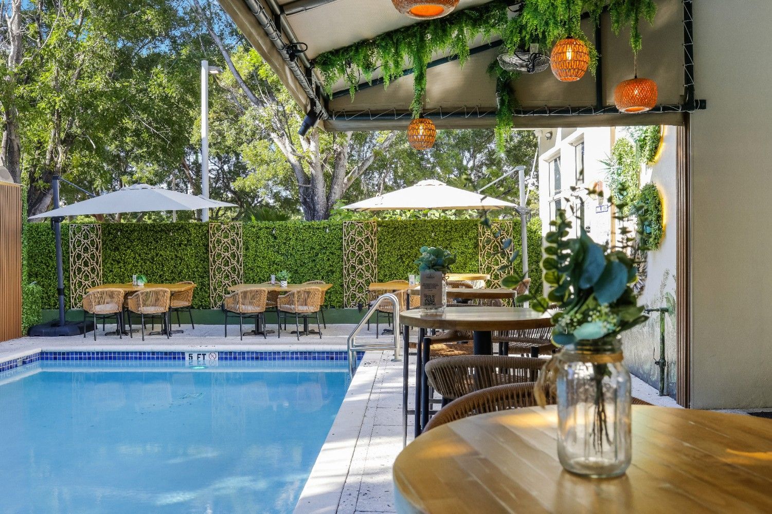 Poolside dining area with tables, umbrellas, a pool, and decorative plants.