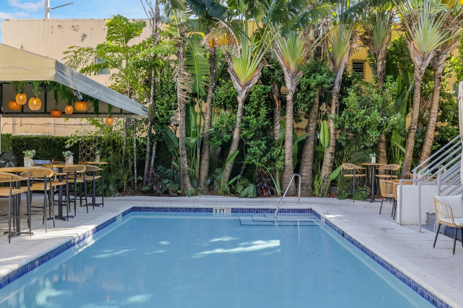 Swimming pool surrounded by tropical plants and tables under a canopy.