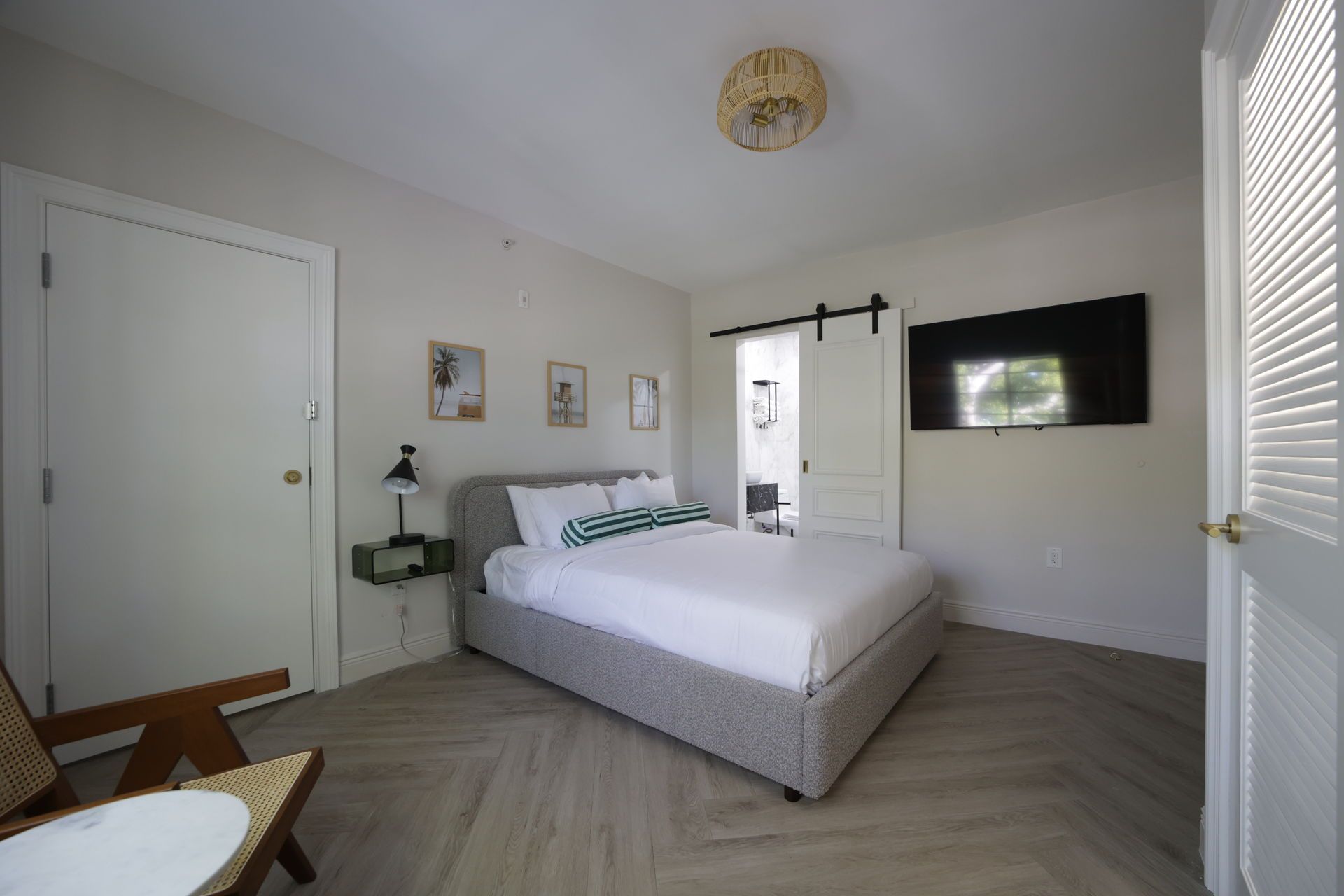 Bedroom with a bed, TV, and open doorway. Light-colored walls and wood flooring.