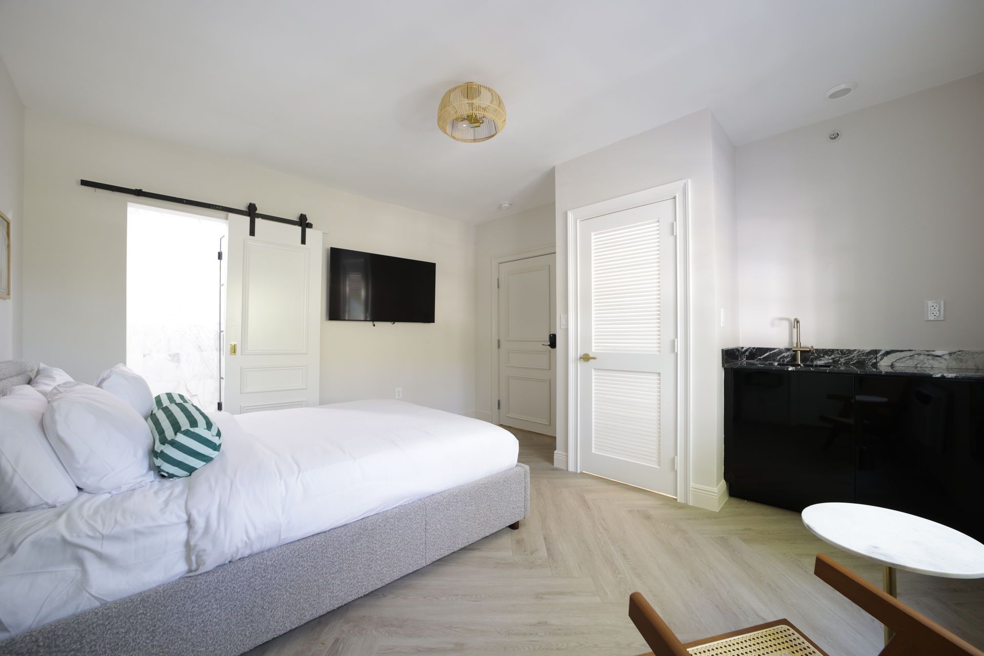 Bedroom with bed, television, and bar. Light wood floors, white walls, and a sliding door.