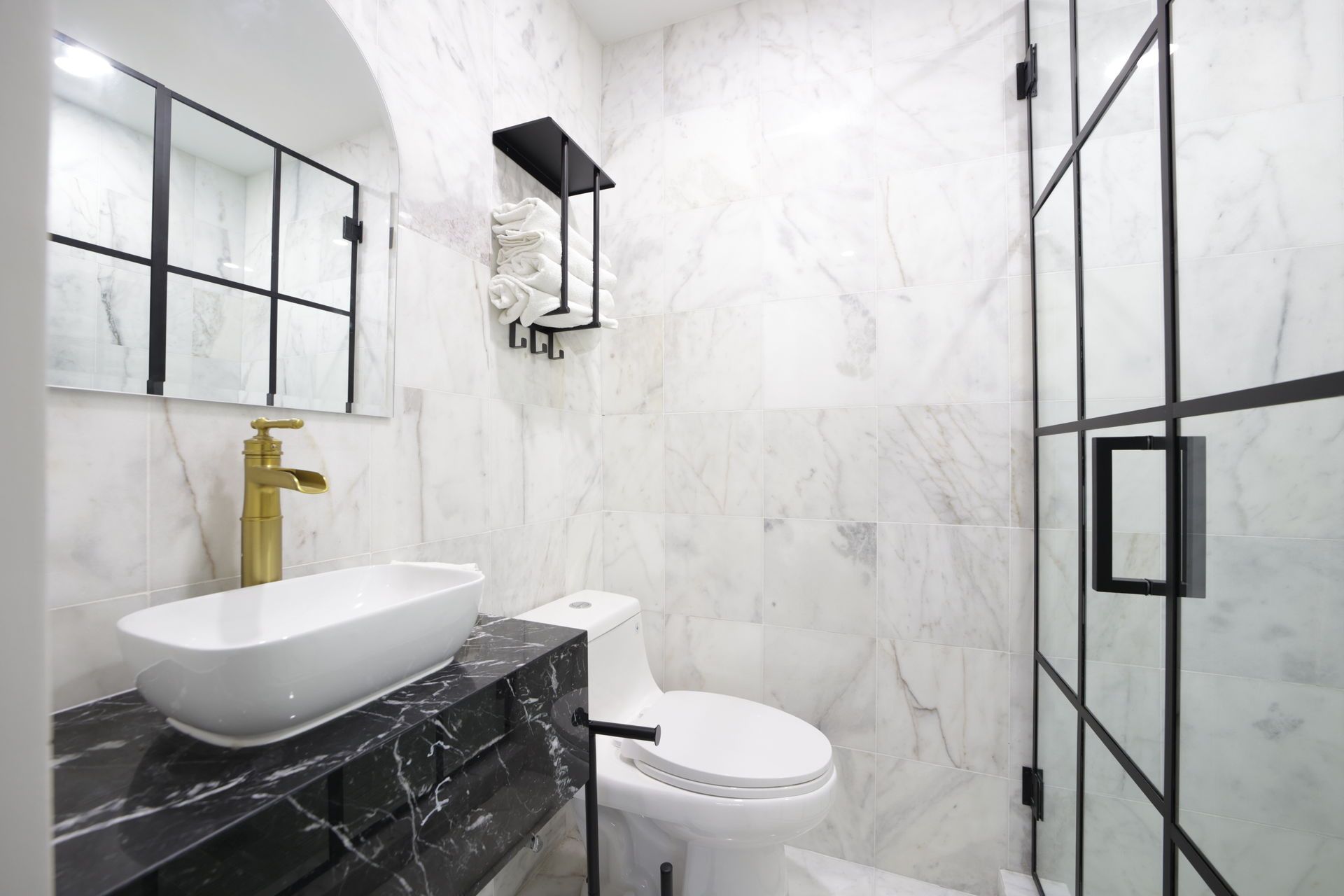 Modern bathroom with marble walls, a gold faucet, black vanity, and black-framed shower.